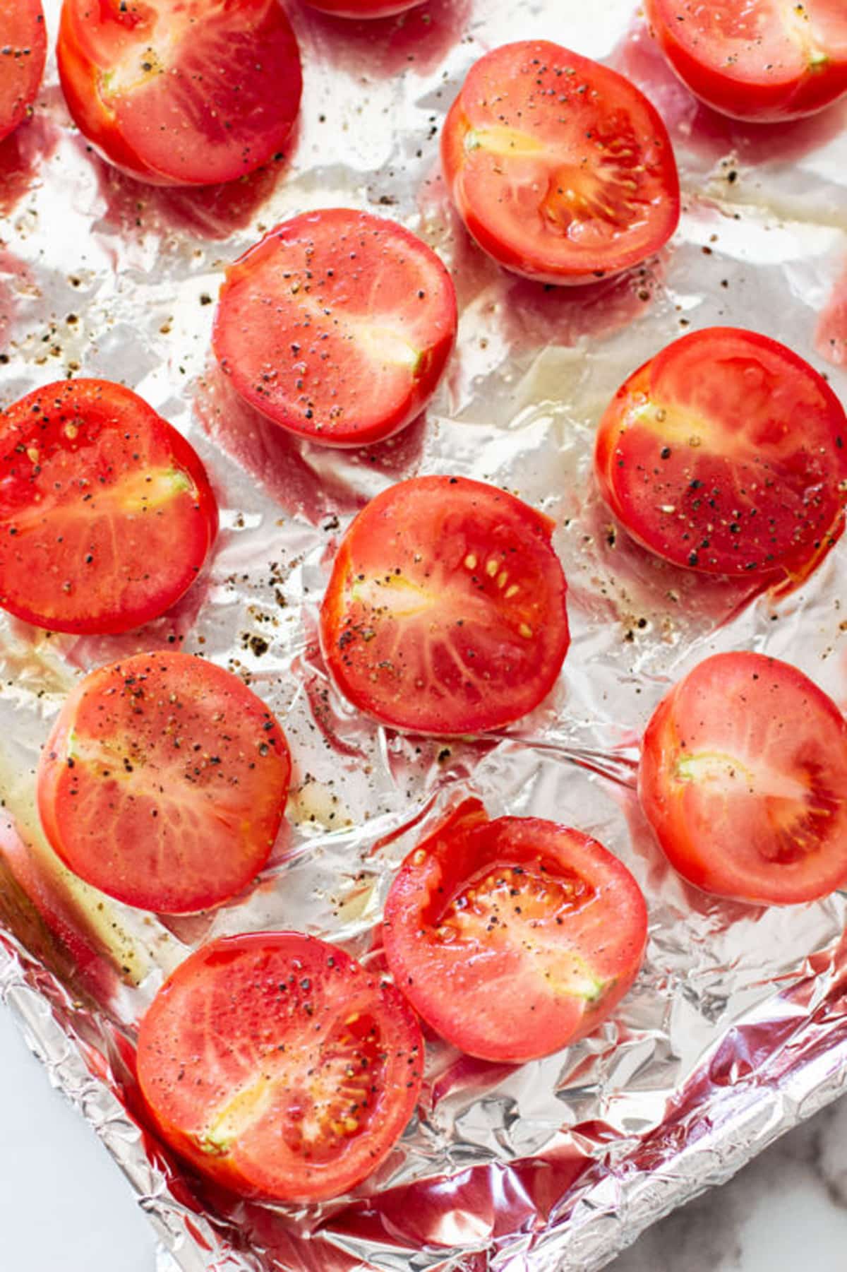 Cookie sheet lined with aluminum foil topped with fresh tomatoes cut lengthwise topped with salt and pepper.