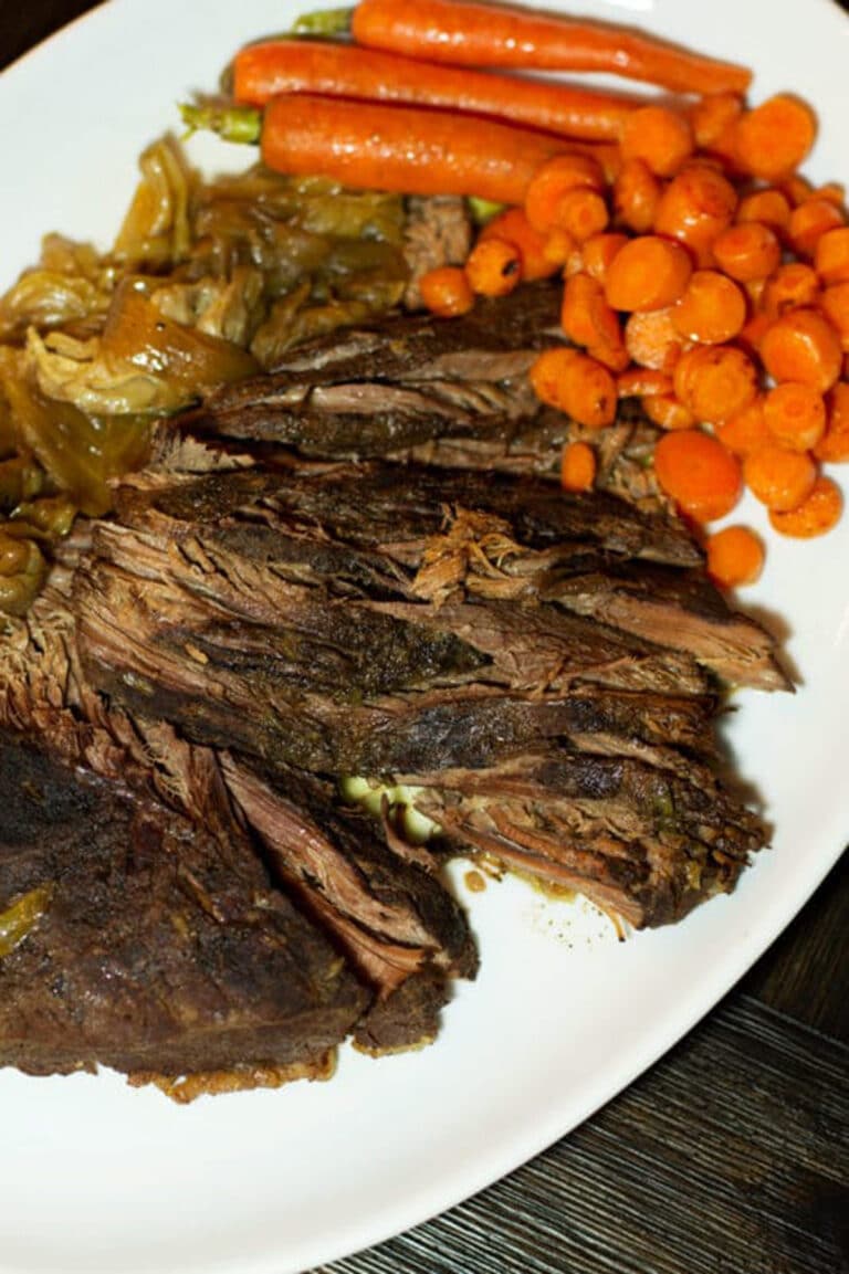 Sliced brisket on a white platter, topped with carrots and cabbage.