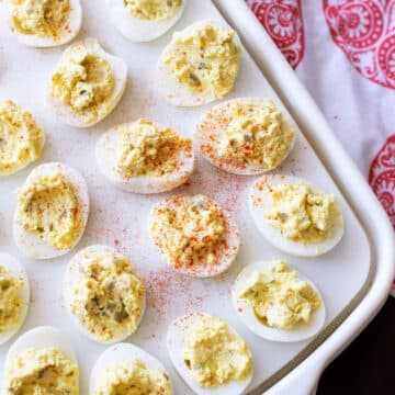 Platter containing 24 deviled eggs sopped with paprika.