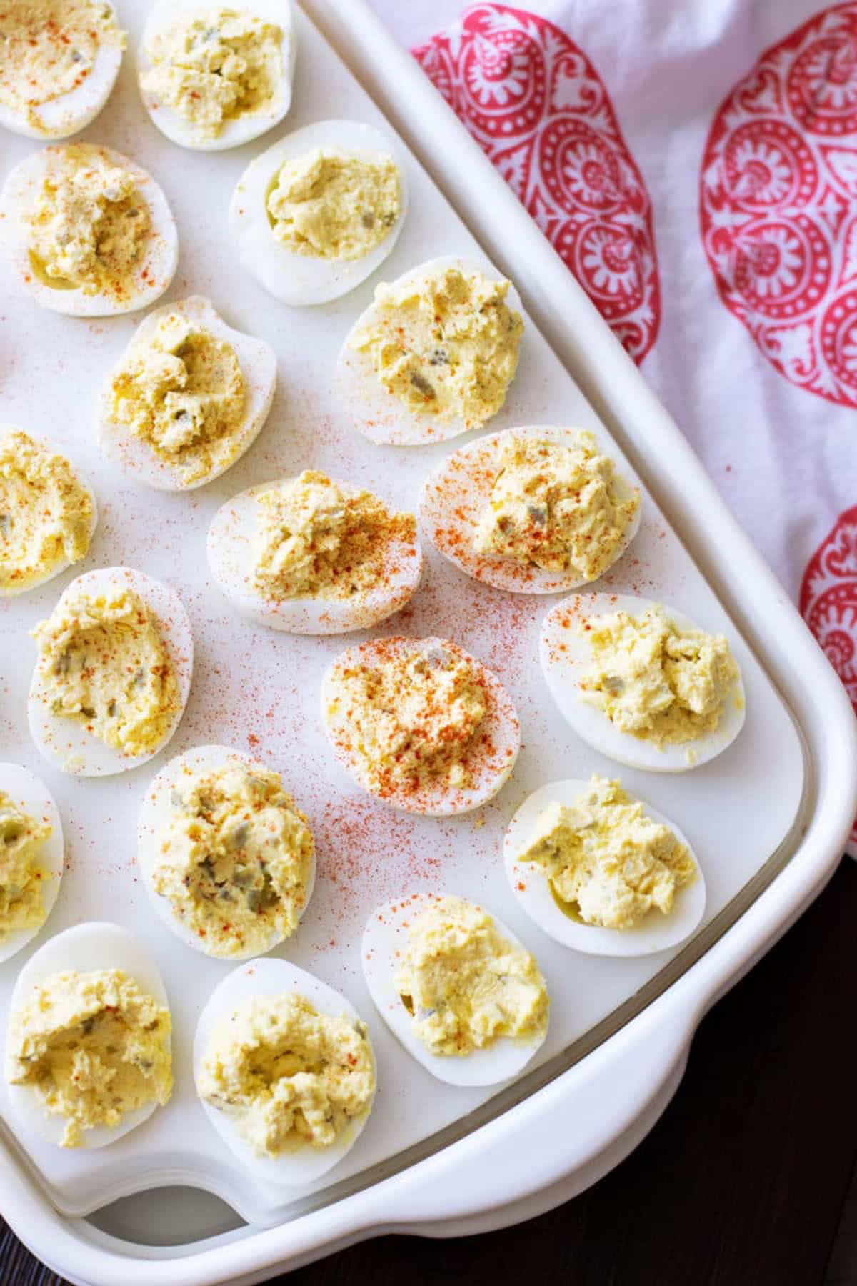 Platter containing 24 deviled eggs sopped with paprika. 
