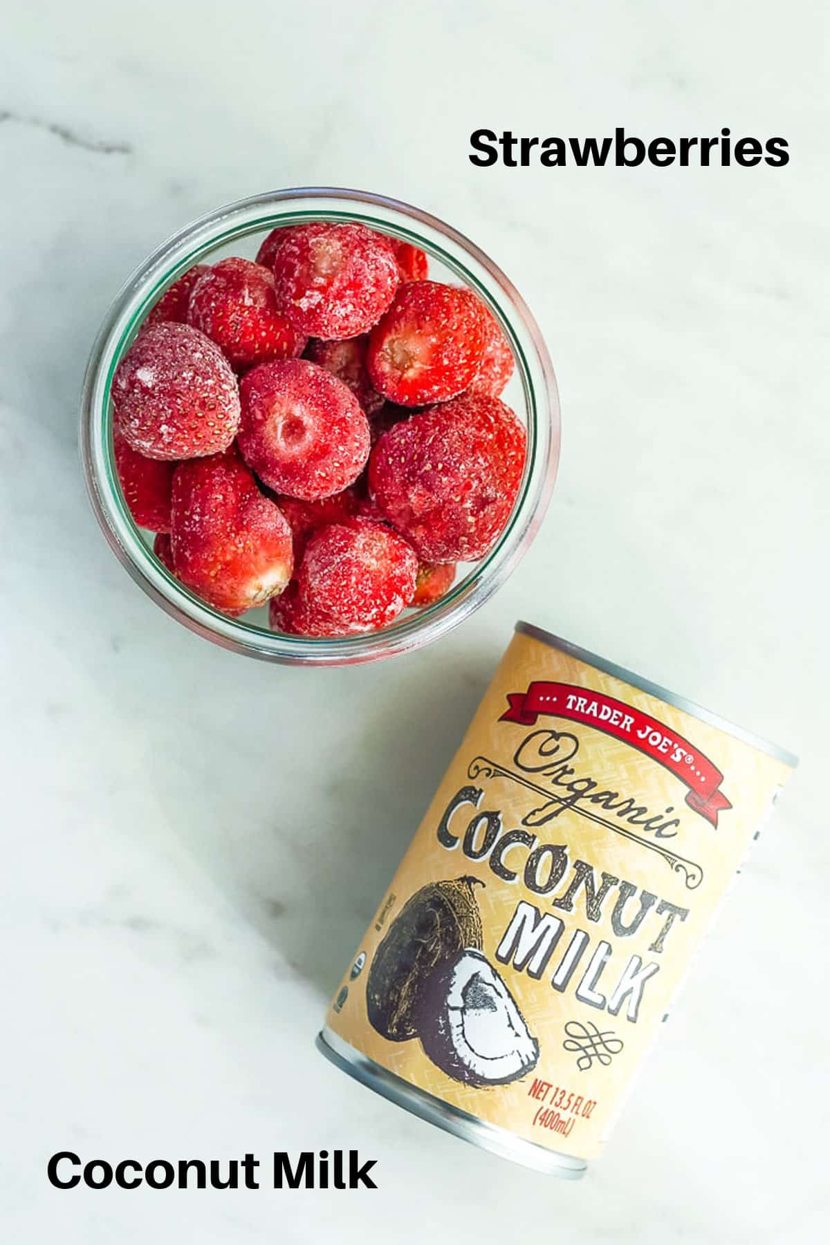 A bowl of frozen strawberries and a can of coconut milk on a white board.
