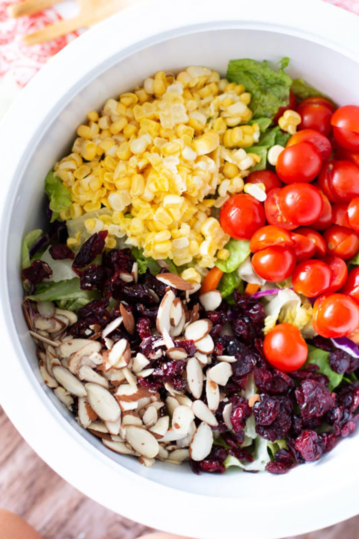 White bowl containing corn, cherry tomatoes, lettuce, almonds, and cranberries.