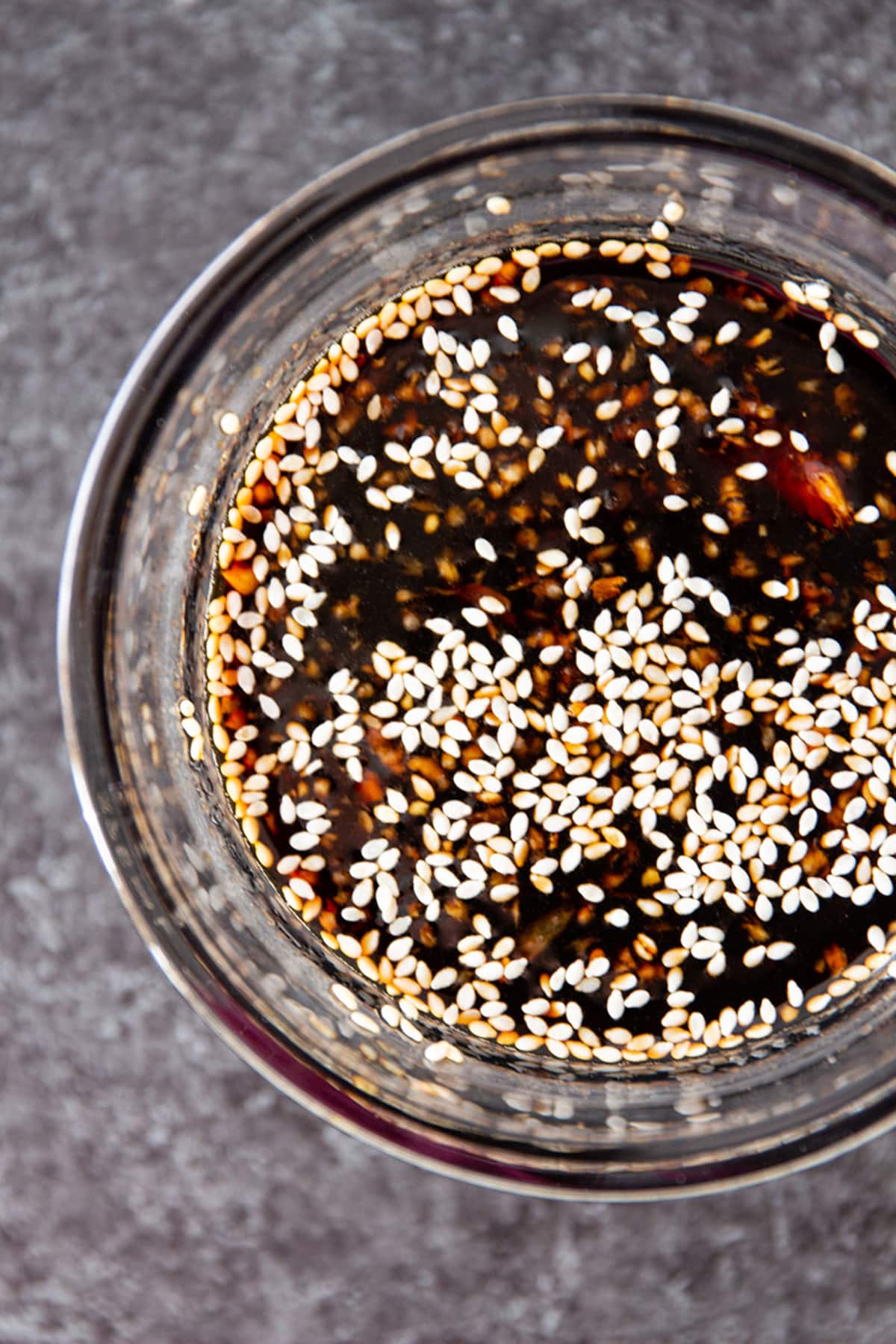 Glass jar containing a teriyaki marinade topped with sesame seeds.