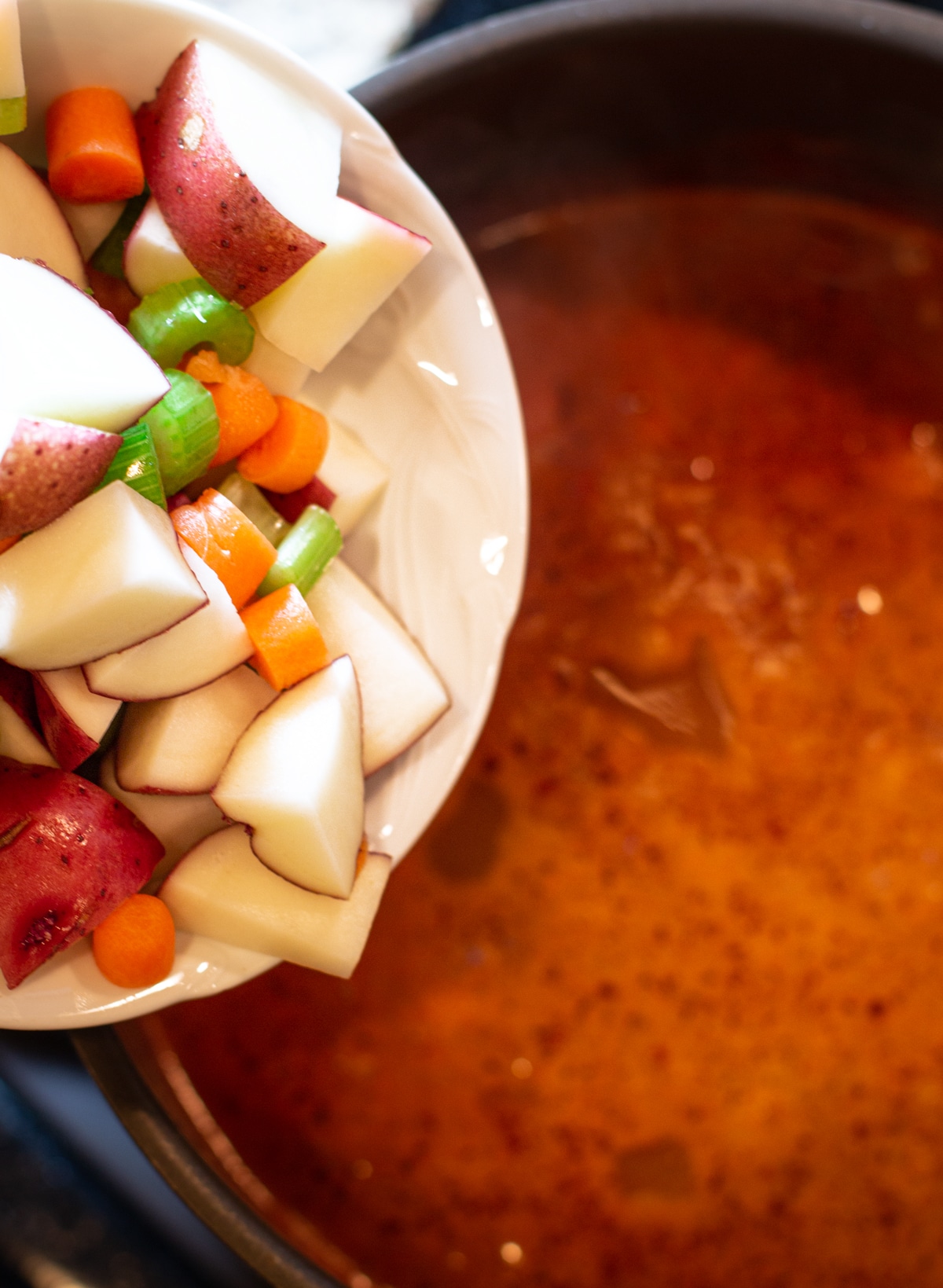 Person adding fresh cut vegetables into a pot of Vegetable Beef Soup.