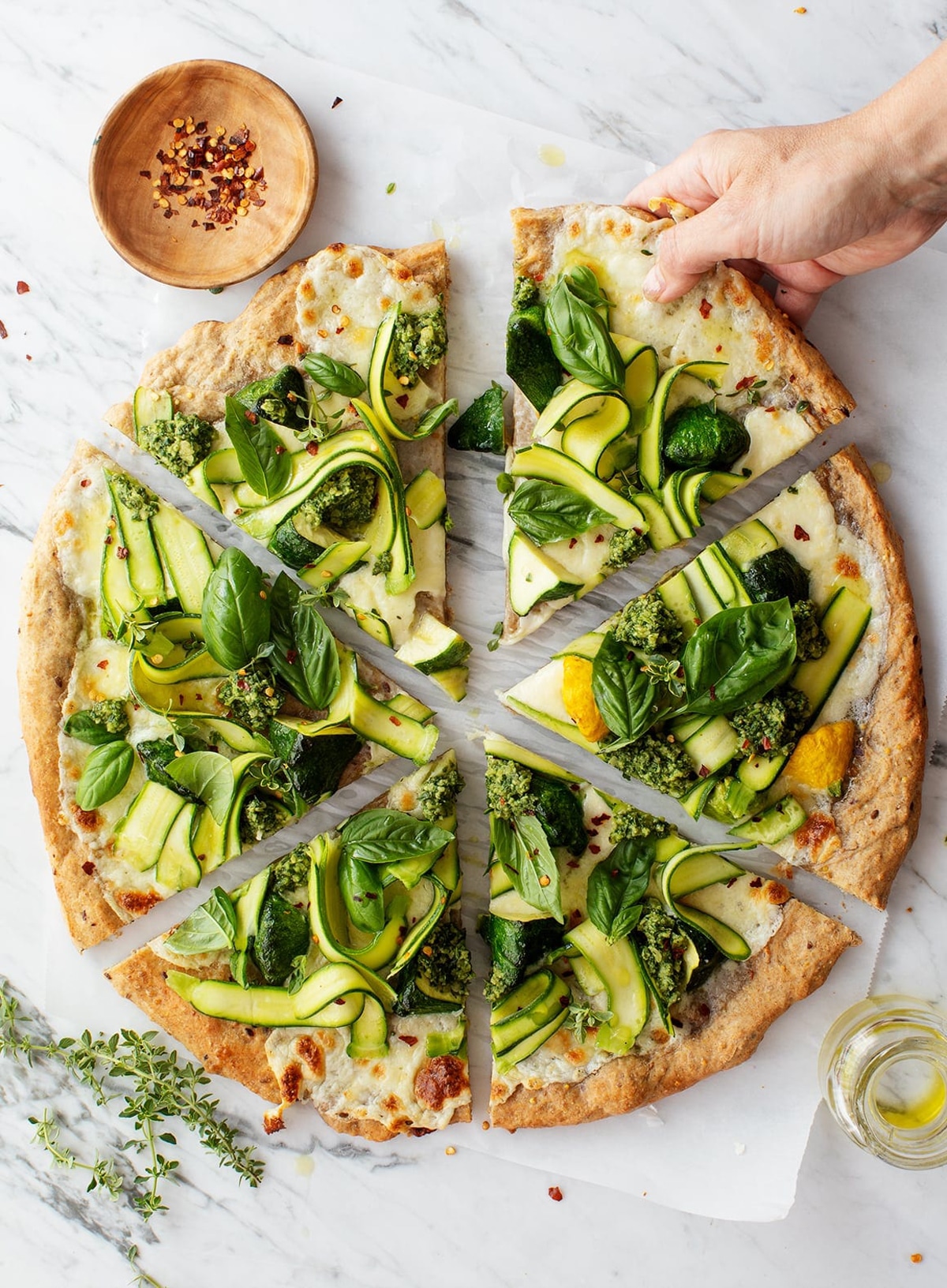 Sliced zucchini pizza on a table, herbs and olive oil on side. 