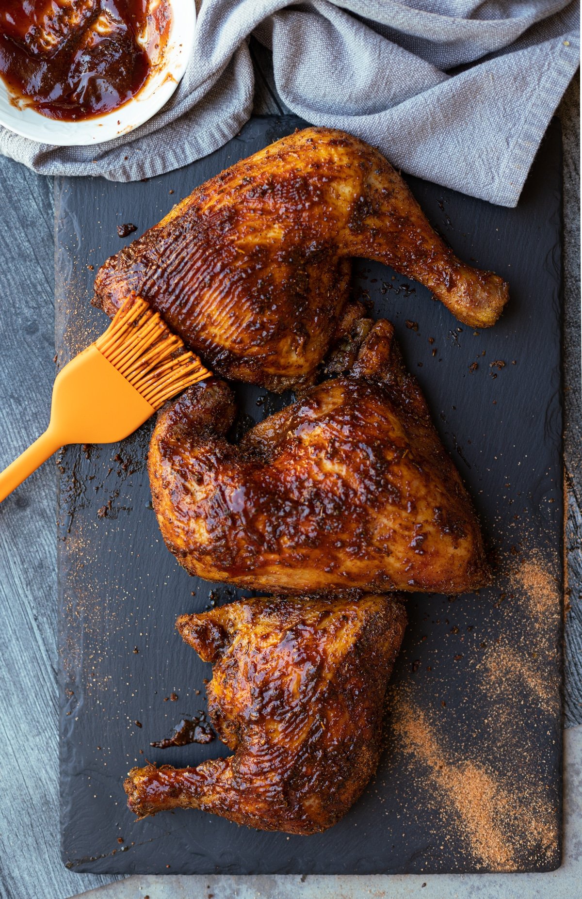 Smoked chicken quarters on a slate plate topped with BBQ sauce.