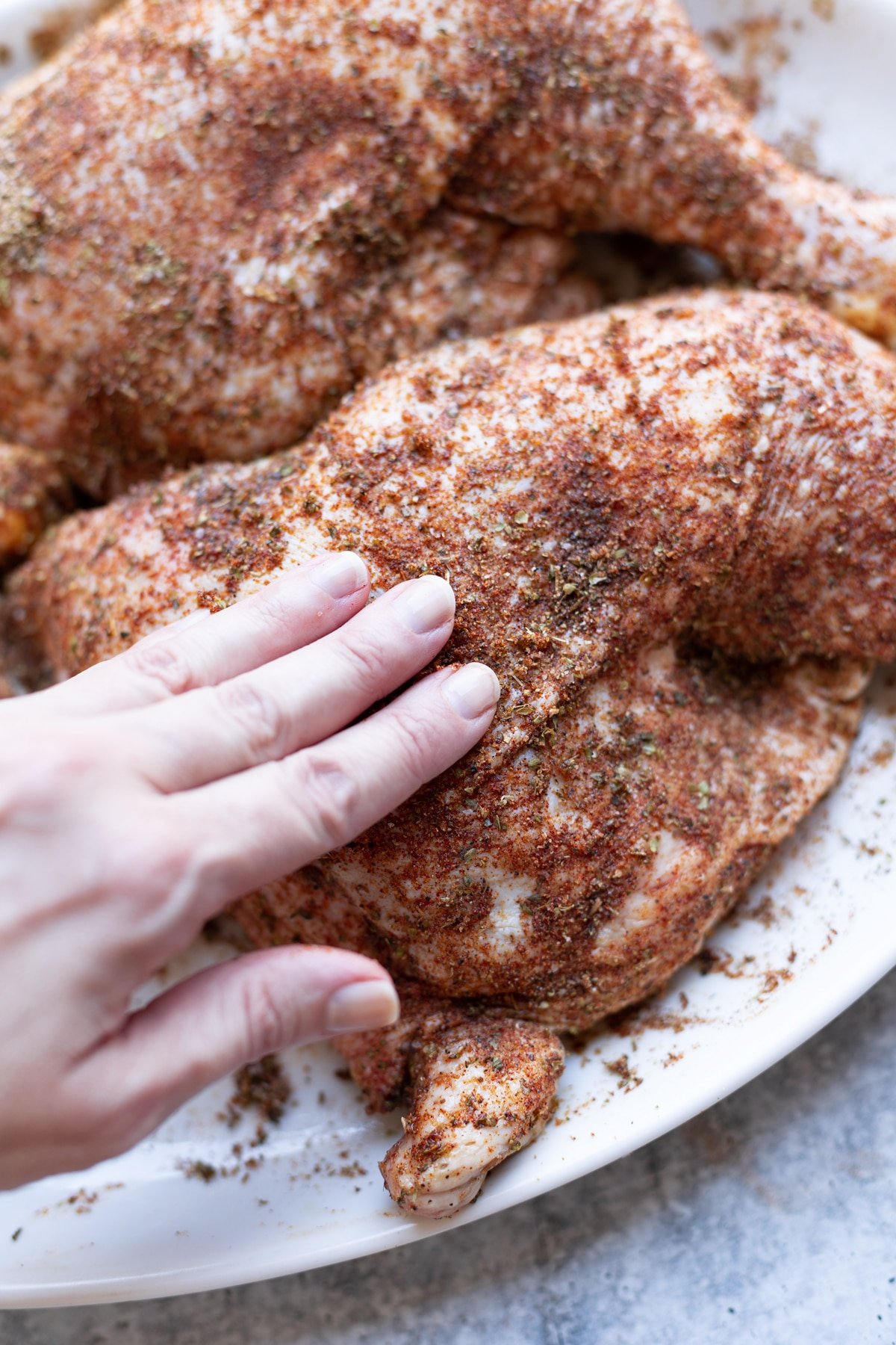 Person using their hand to apply BBQ rub to chicken.