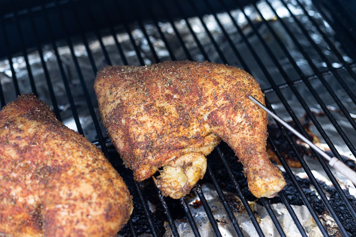 Chicken quarter on smoker racks with internal meat thermometer in the leg. 