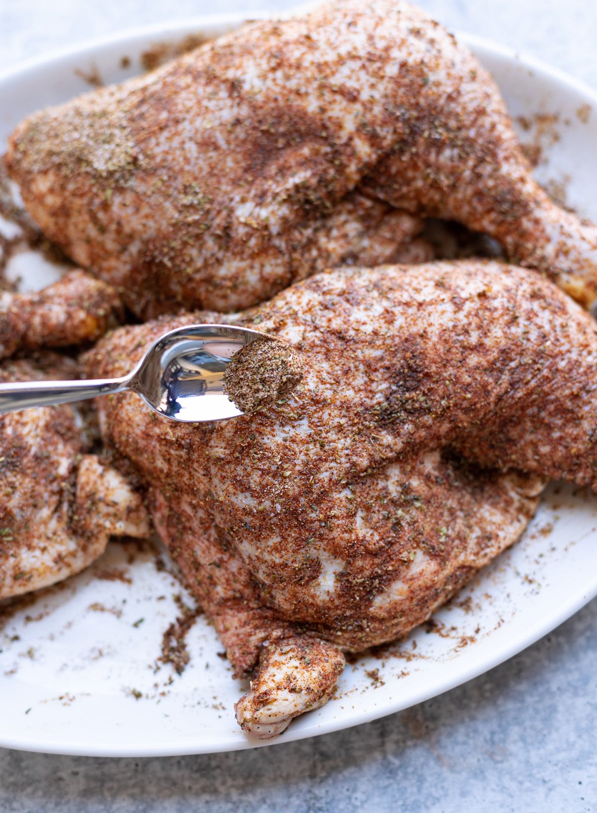 Spice mixture being applied to chicken with a spoon.