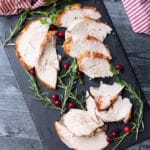 Sliced turkey breast on a plate, cranberries and rosemary on table.