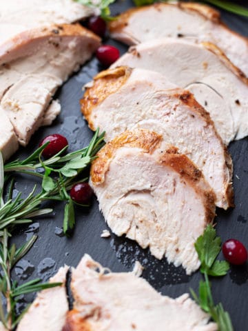 Sliced turkey on a platter, rosemary and cranberries on side.