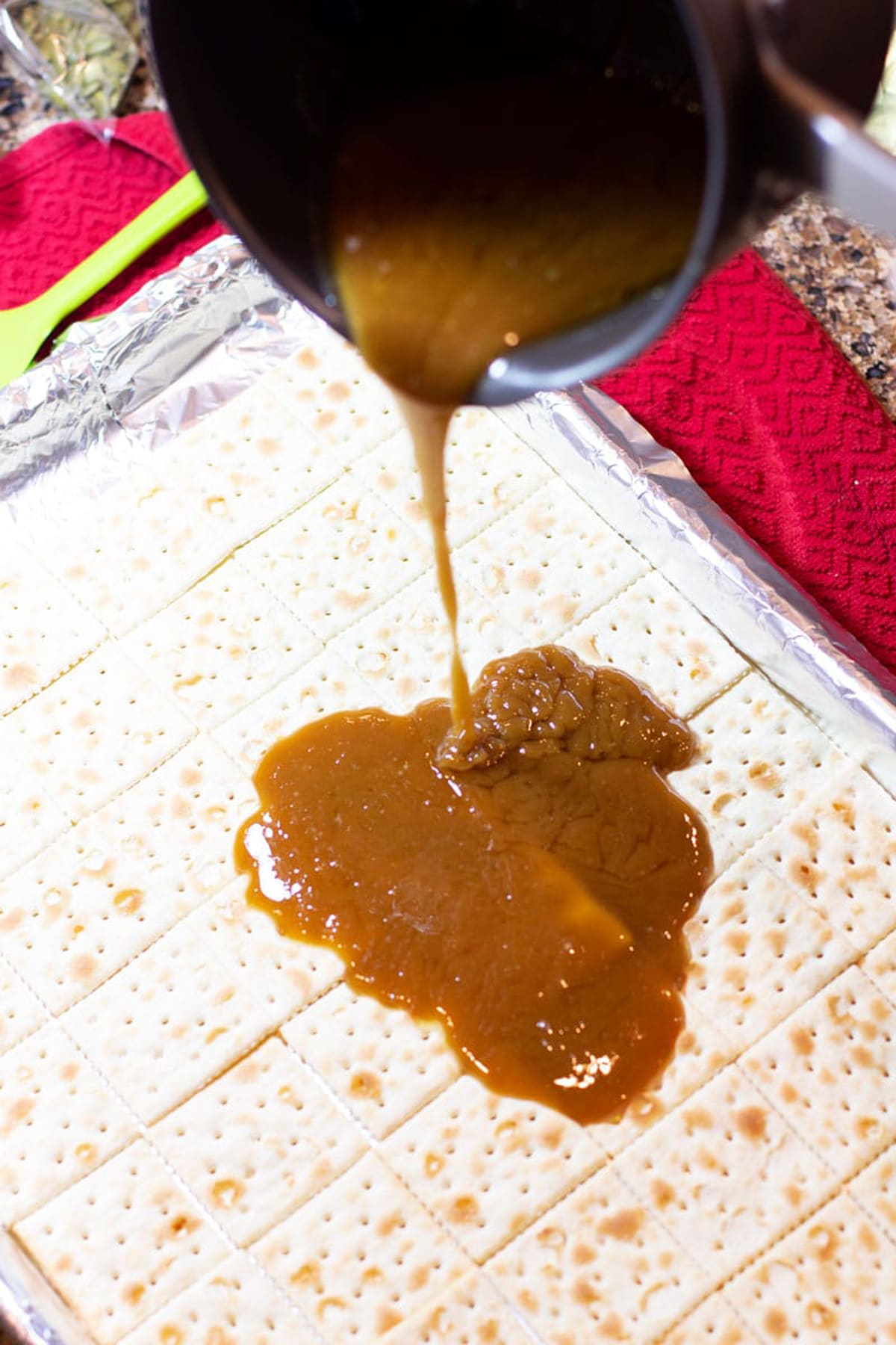 Caramel sauce being poured onto a cookie sheet of saltine crackers. 