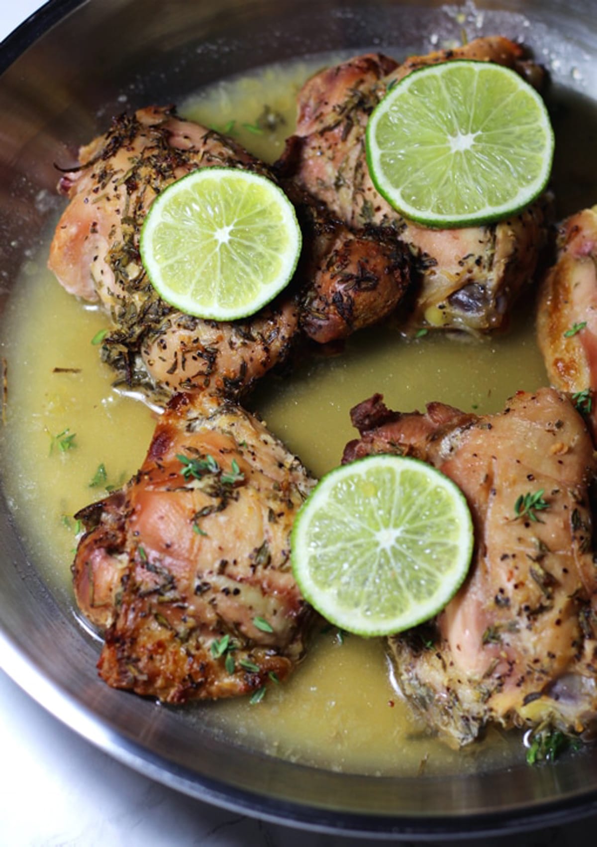 Silver pan containing 5 Lemon Thyme Chicken thights with Garlic and Rosemary, topped with lime slices.