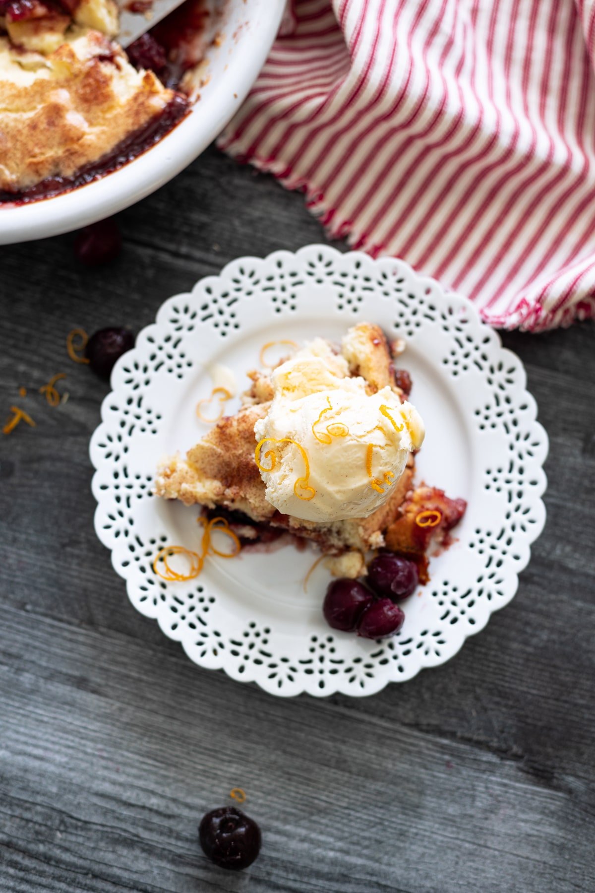 Piece of cherry pie on a plate topped with vanilla ice cream.