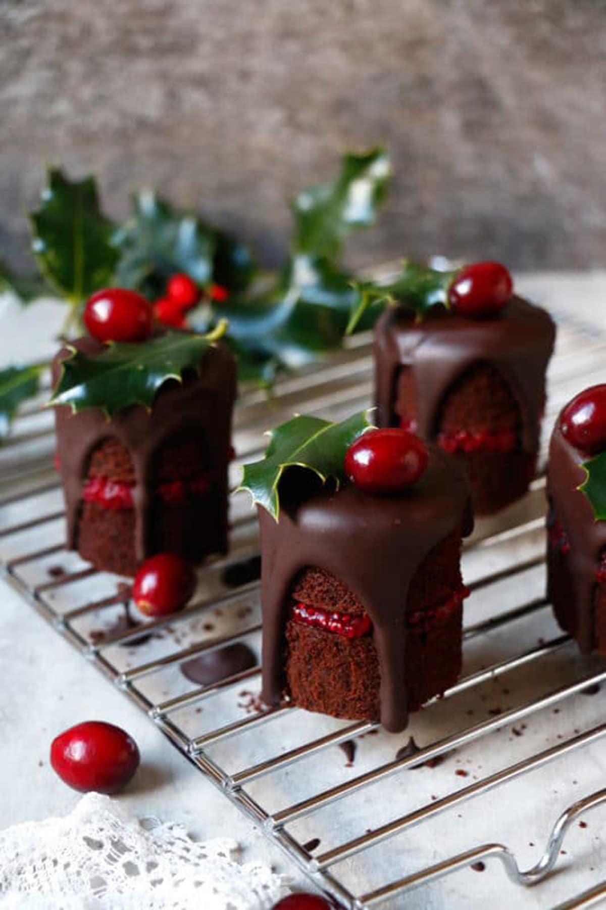 Little brownies stacked on top of each other that have fudge over them topped with cranberries. 