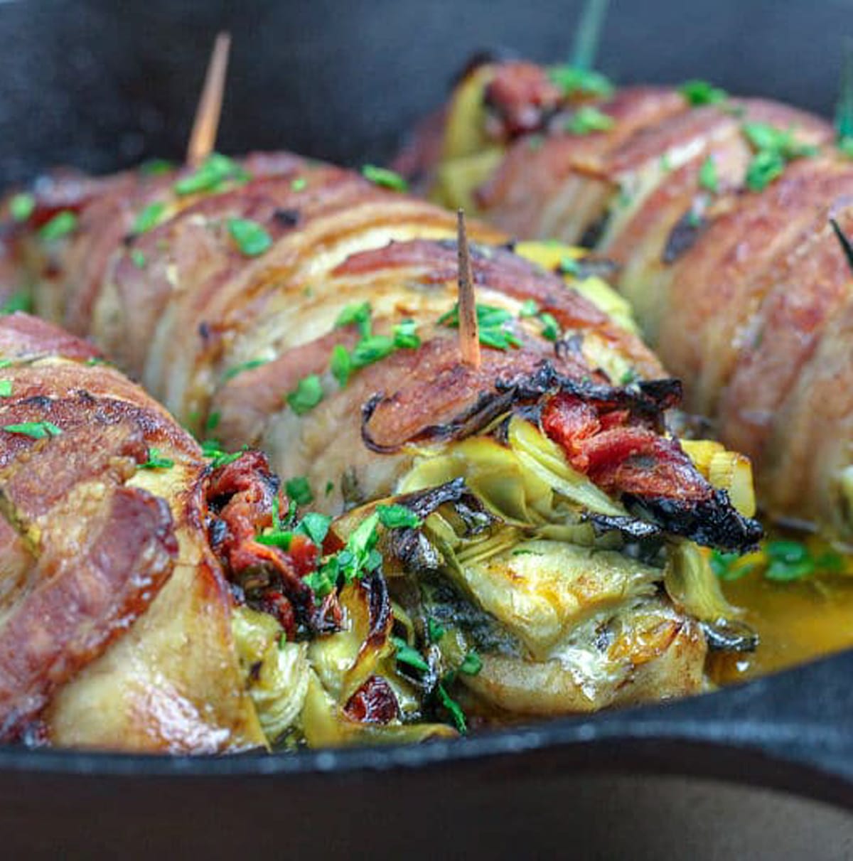 Stuffed Chicken wrapped in bacon cooked in a skillet. 