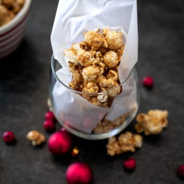 Bowl of Bourbon Caramel Popcorn sitting on a black table, red Christmas balls on table by red tablecloth.