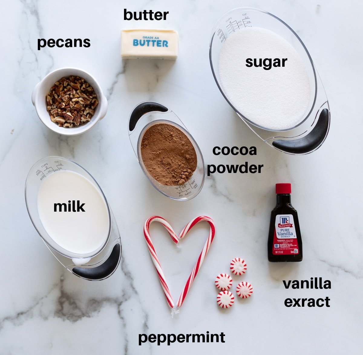 milk, sugar, cocoa powder, vanilla extract, nuts, and peppermint on a counter.