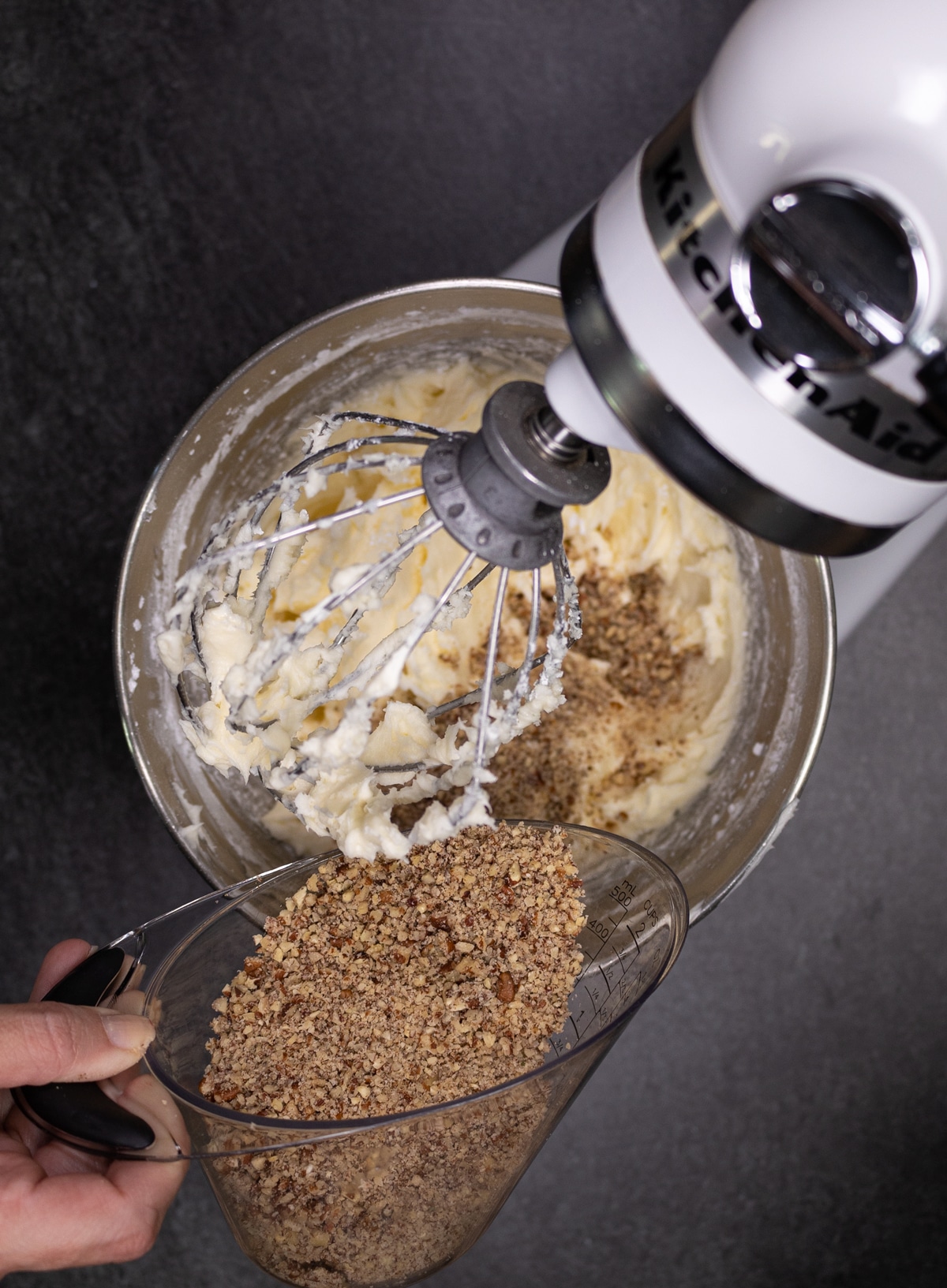 person pouring in chopped pecans into a standing mixer for making cream cheese frosting. 