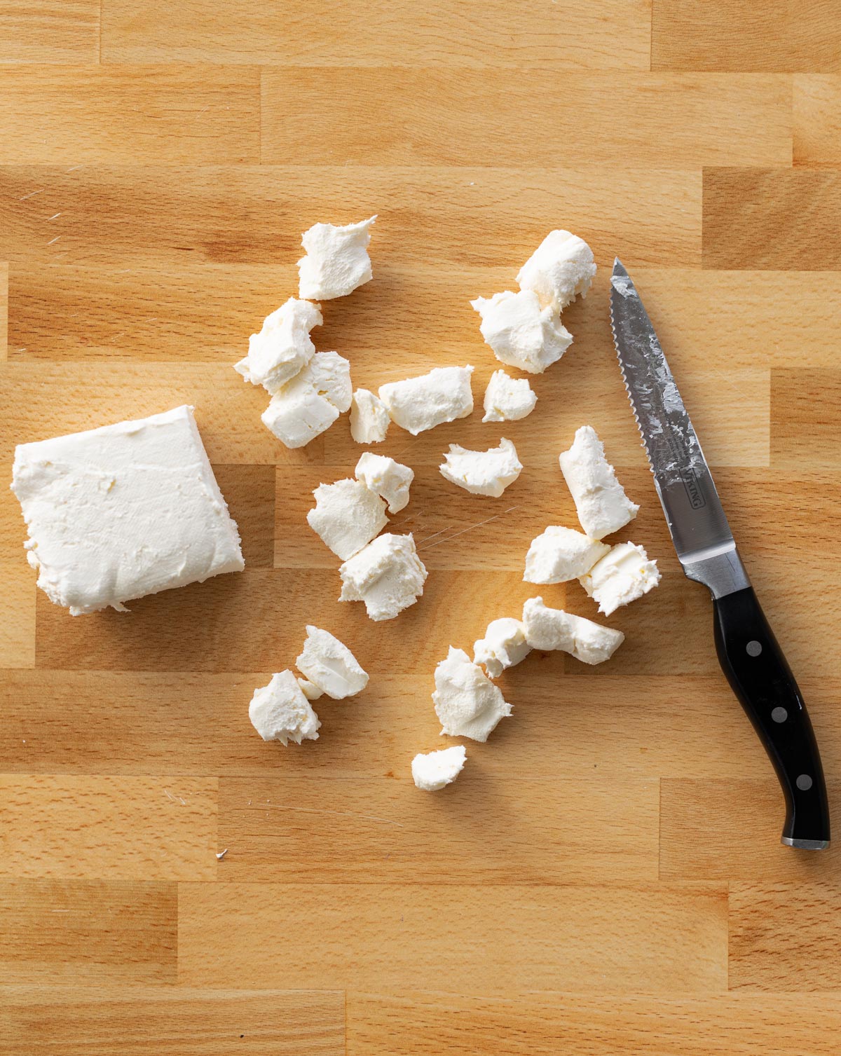 Knife on a counter with cream cheese cut into cubes. 