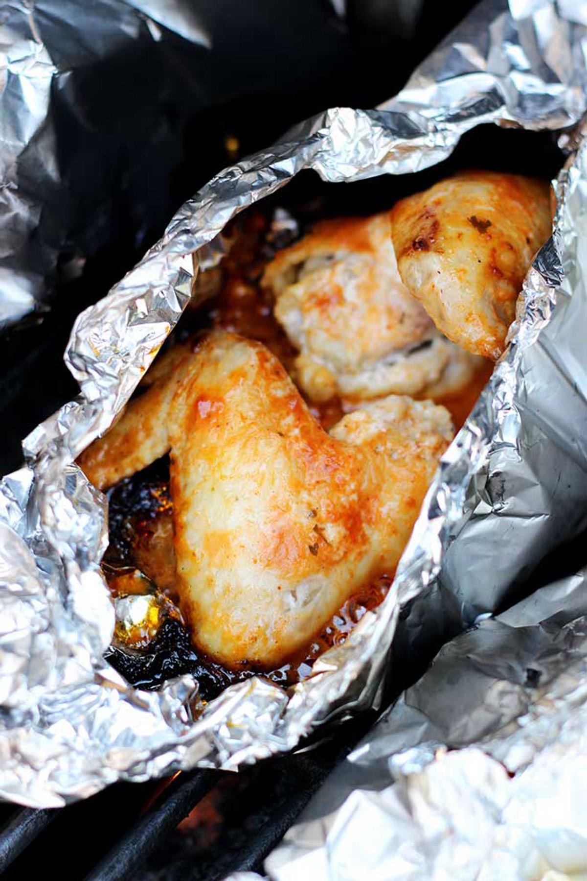 Aluminum foil pocket containing 2 BBQ chicken wings cooking on a grill.