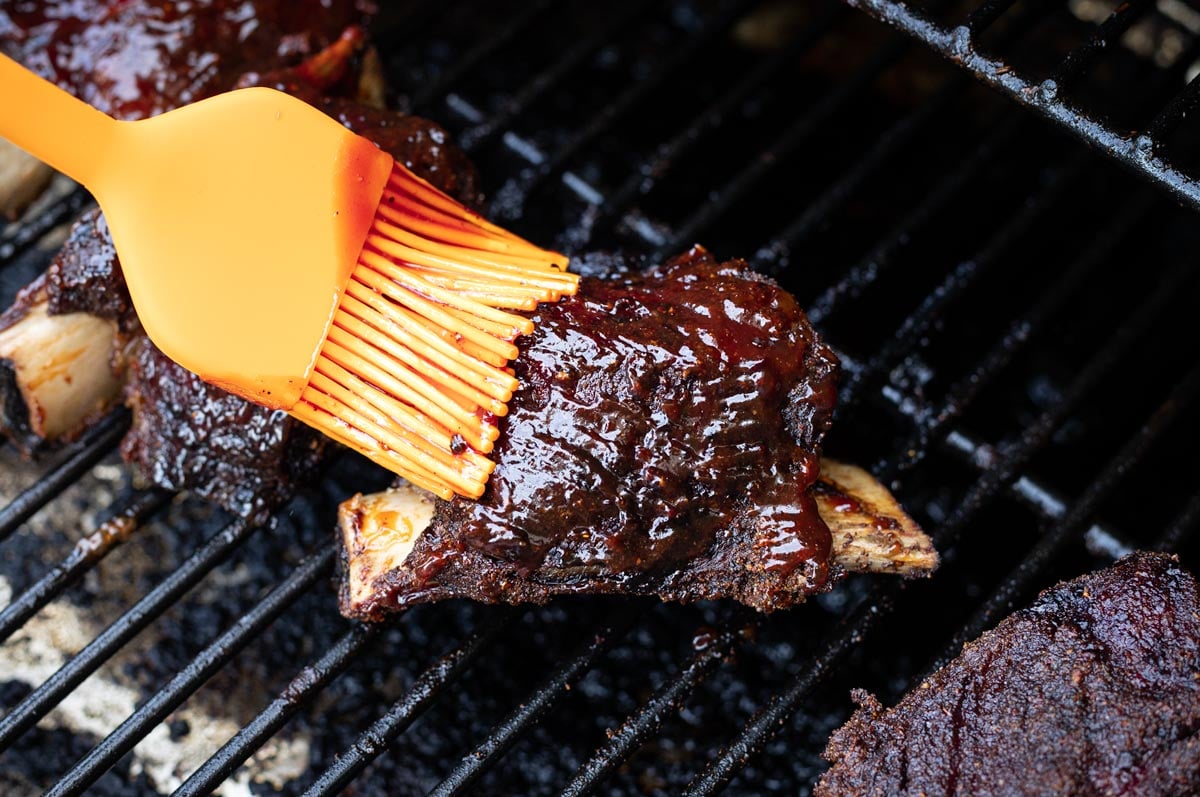 Person basting BBQ sauce on a smoked beef short rib. 