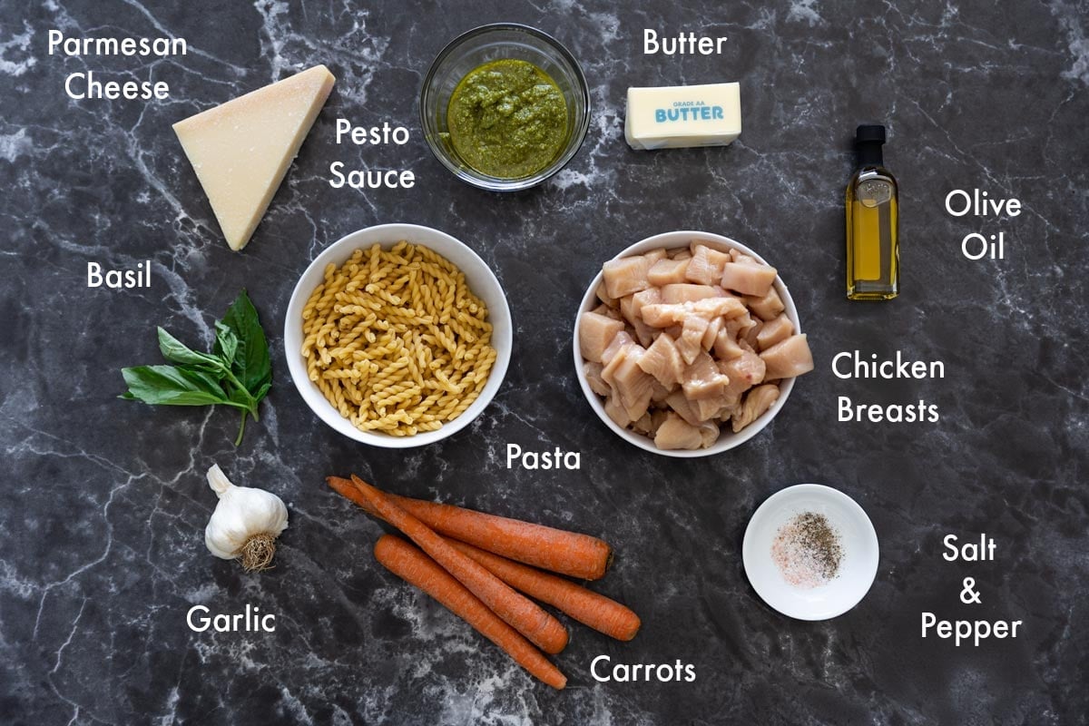 pasta, diced raw chicken, pesto sauce,, and other ingredients on a counter to make parmesan pasta. 