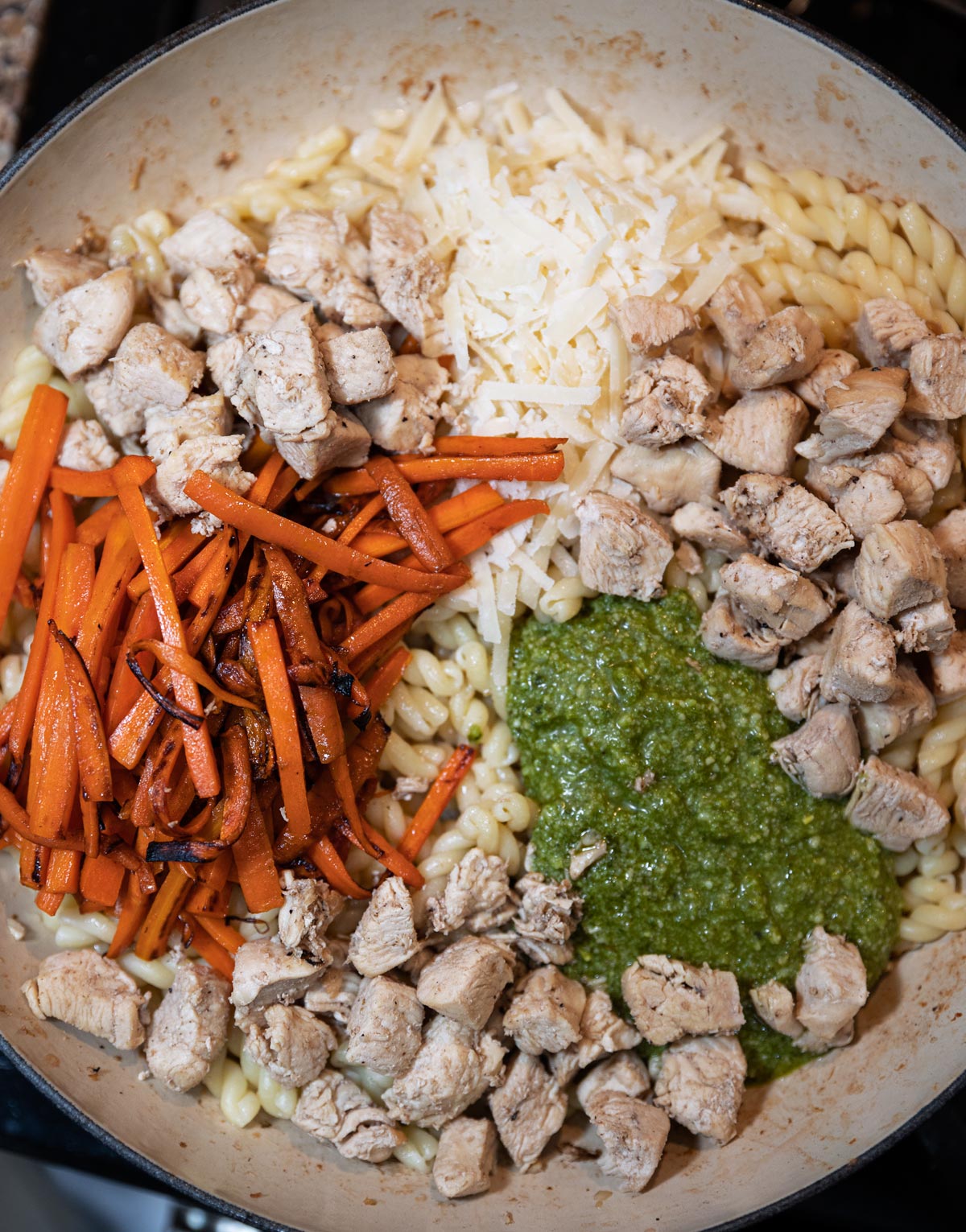 Pasta, chicken, carrots,, parmesan cheese, and pesto sauce in a skillet. 