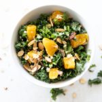 A bowl of orange and kale salad on white table.