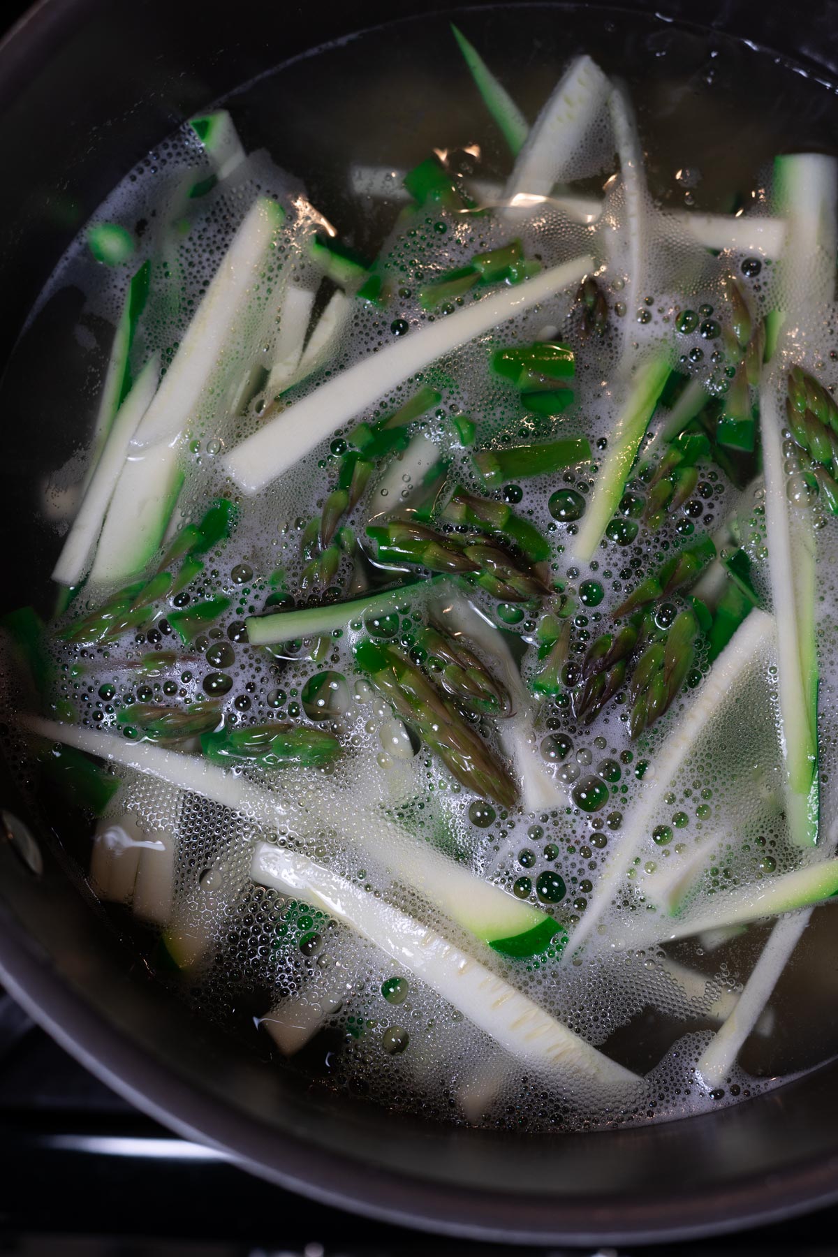 Pasta boiling in a pot of water while asparagus and zucchini blanching. 