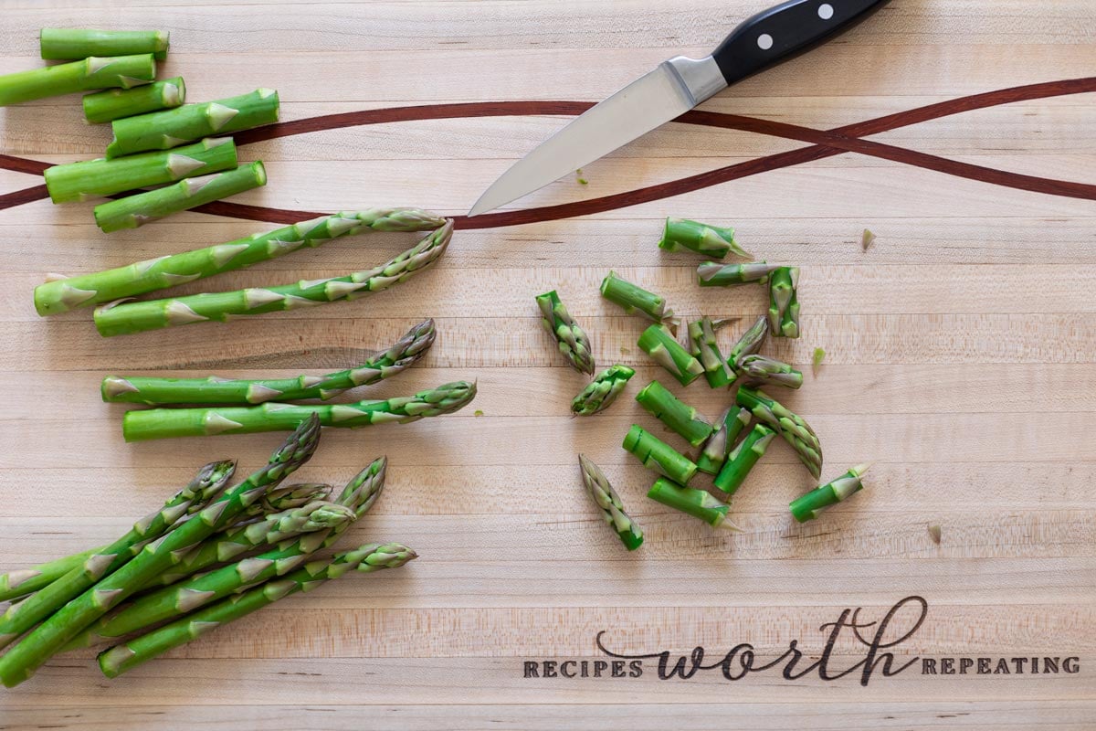 Person cutting fresh asparagus on a cutting board into bite-sized pieces.