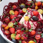 Spiralized beets with sliced cherry tomatoes, block of cream cheese in a bowl.