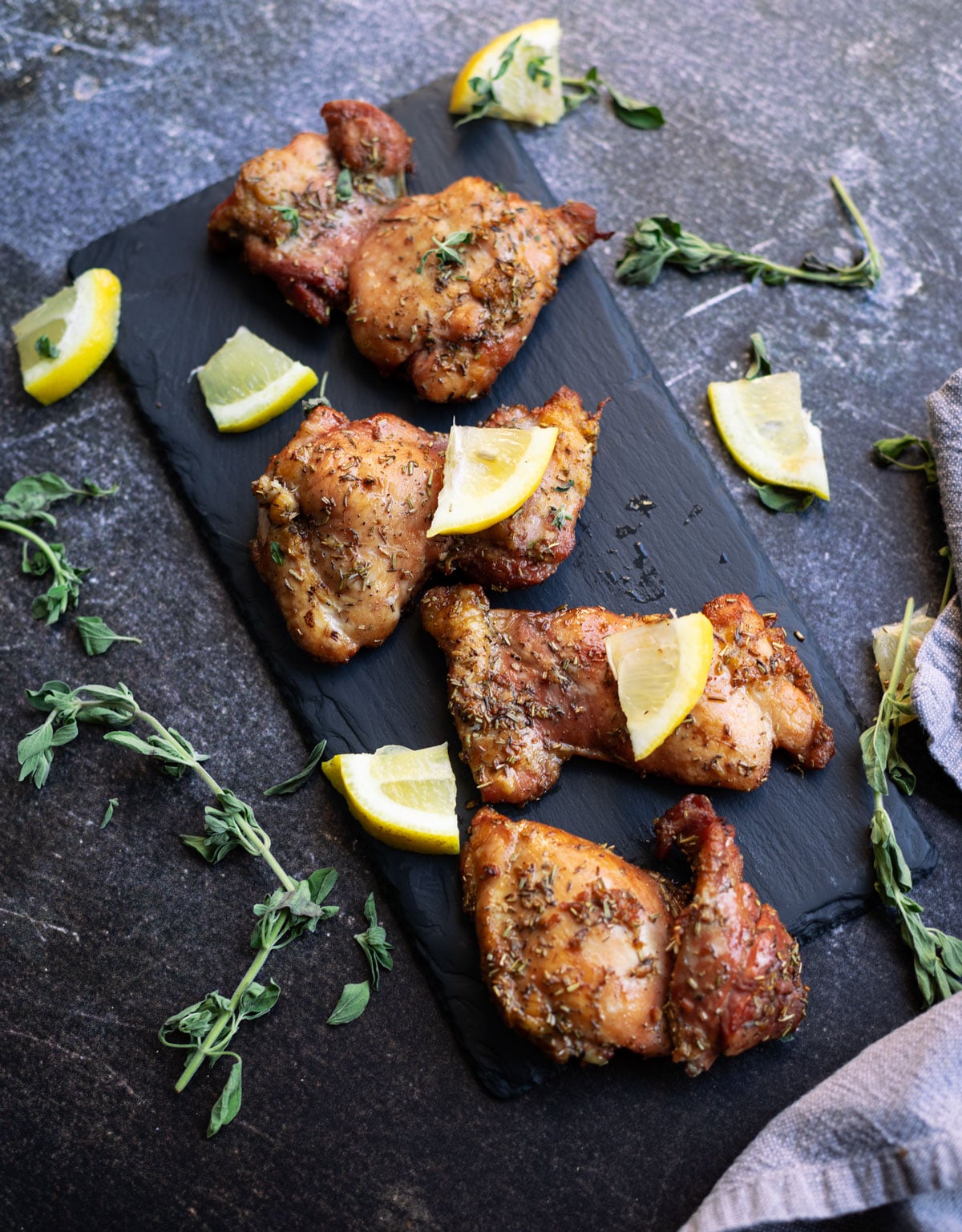 Pieces of chicken thighs on a slate plate, lemons on side. 