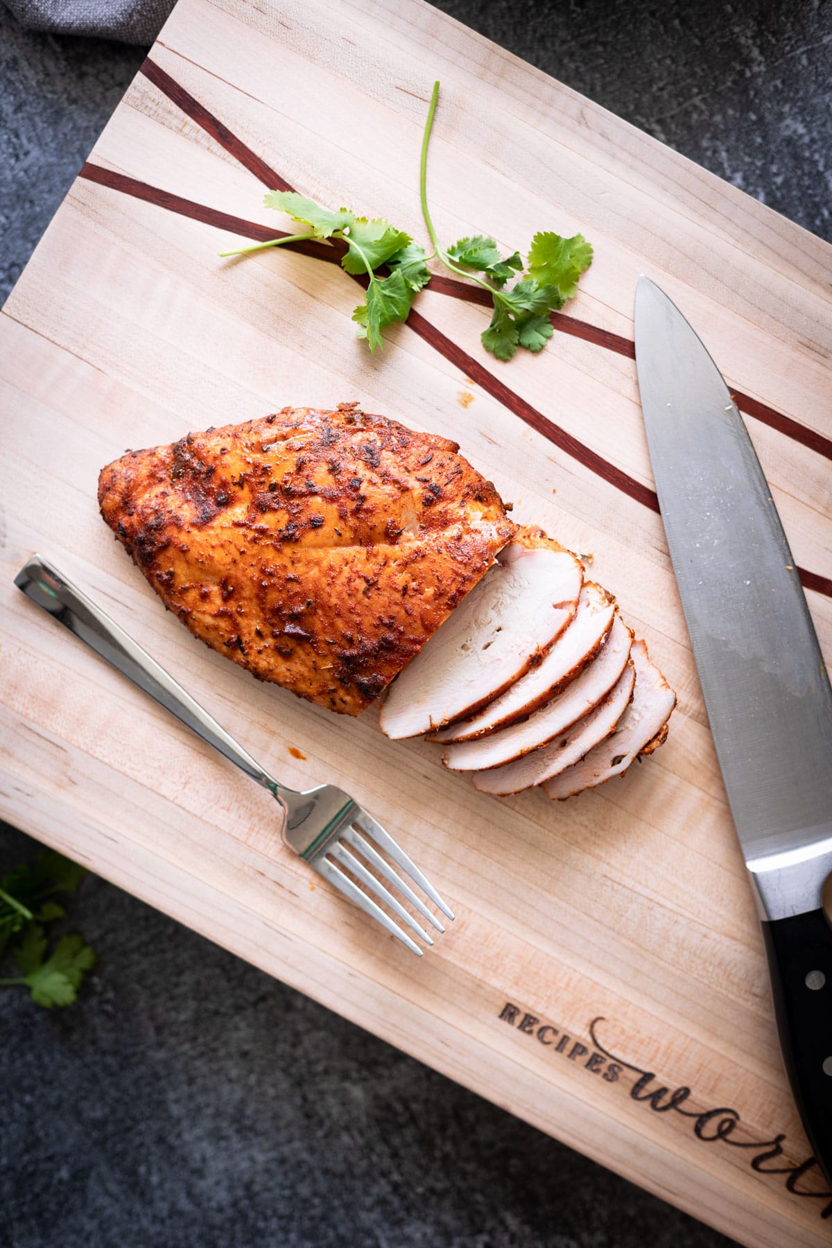 Sliced chicken breast on a cutting board, fork and knife on board.