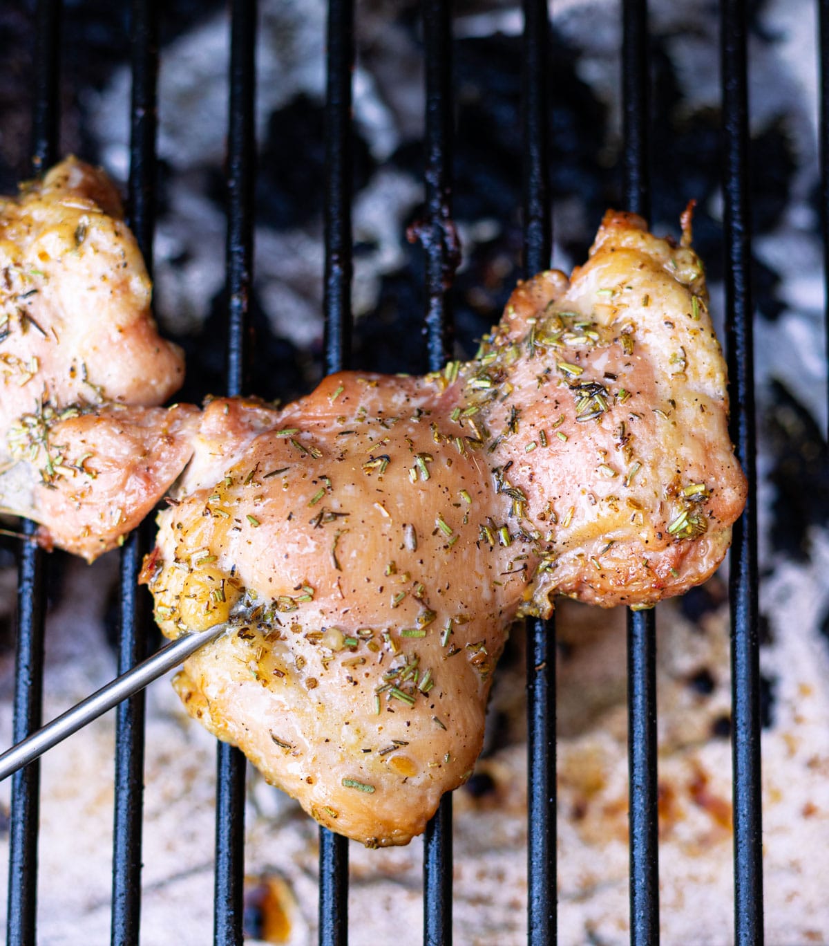 Meat thermometer inserted into chicken thigh on a smoker. 