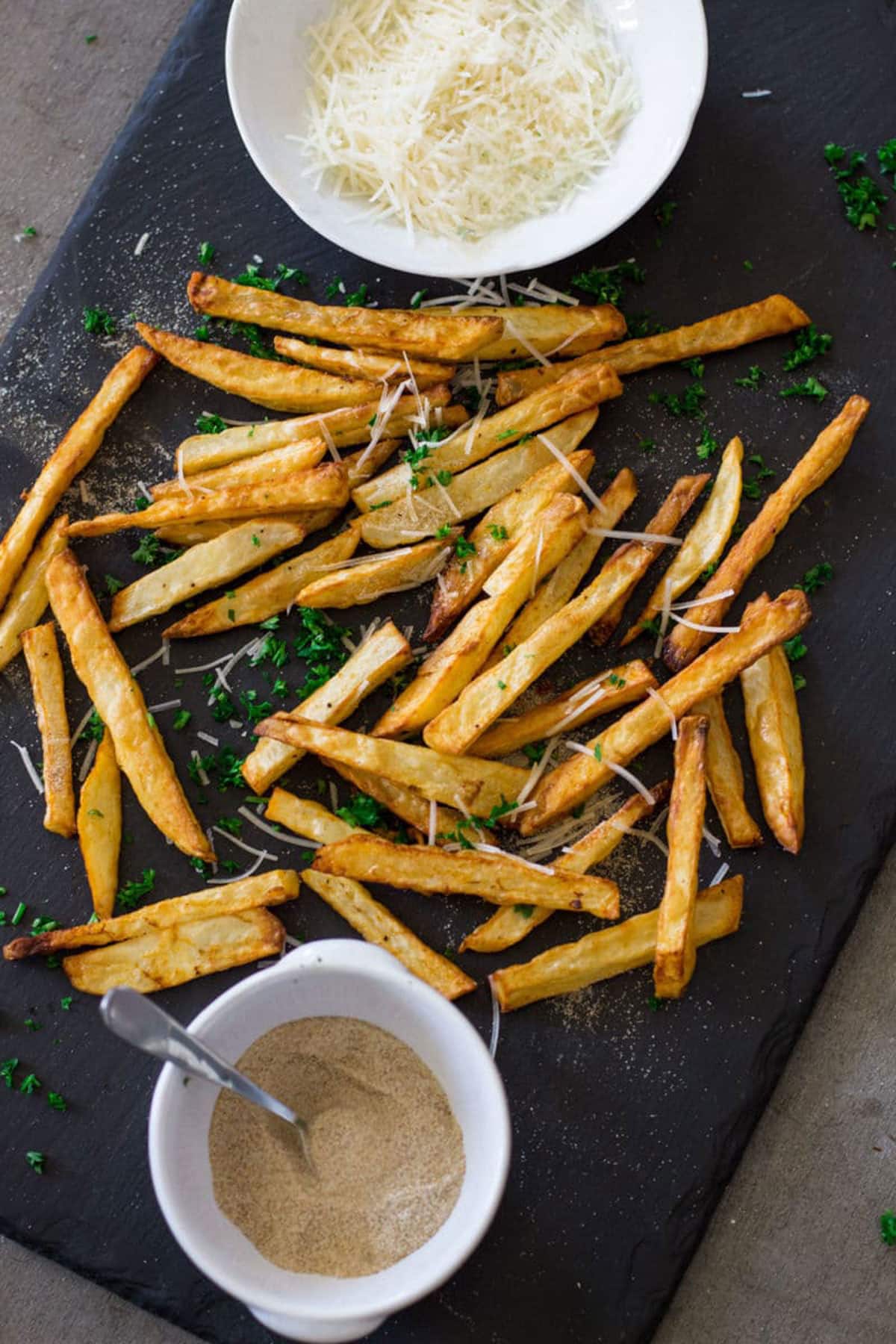 Black serving board containing air fryer french fries topped with Parmesan cheese and seasonings. 