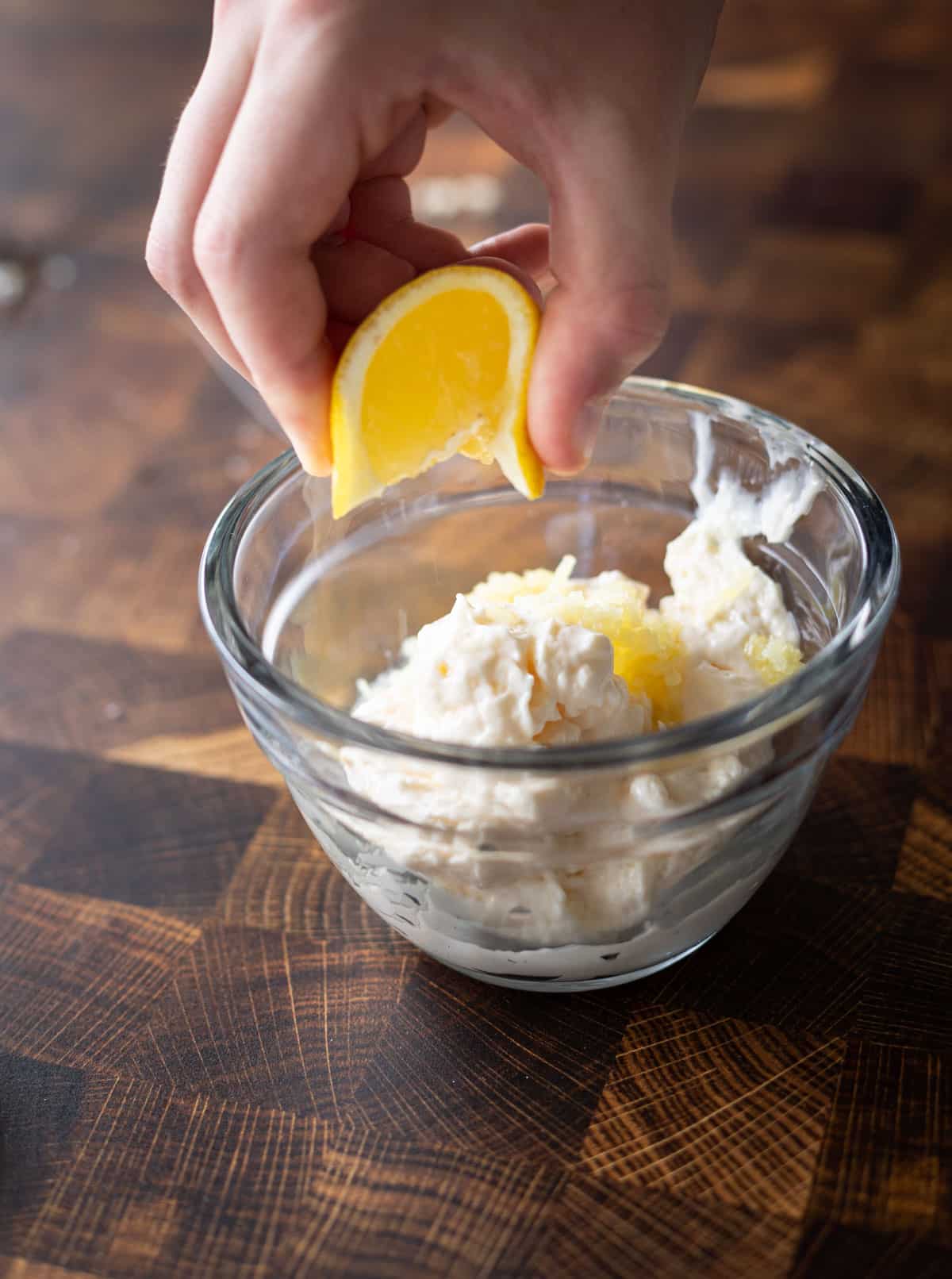 Person squeezing lemon juice into a bowl of mayonnaise. 