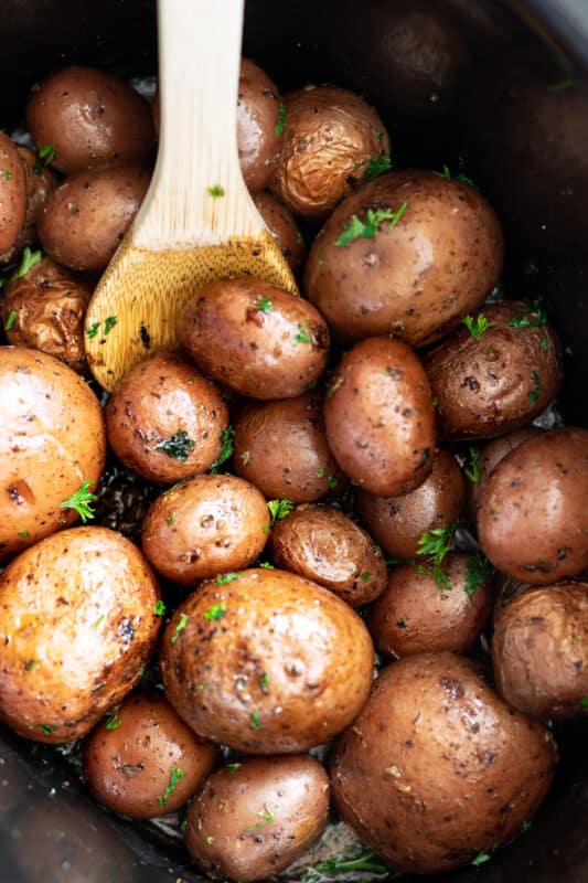 Person stirring potatoes in a large crock pot covered in herbs.