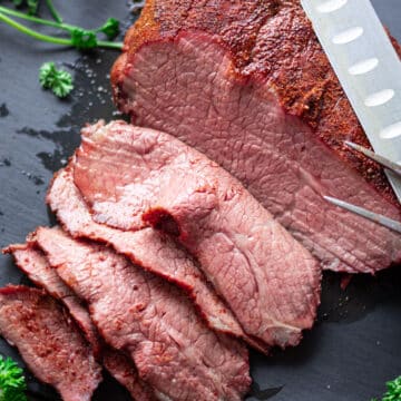 Closeup of smoked Tri Tip on a black slate being sliced.