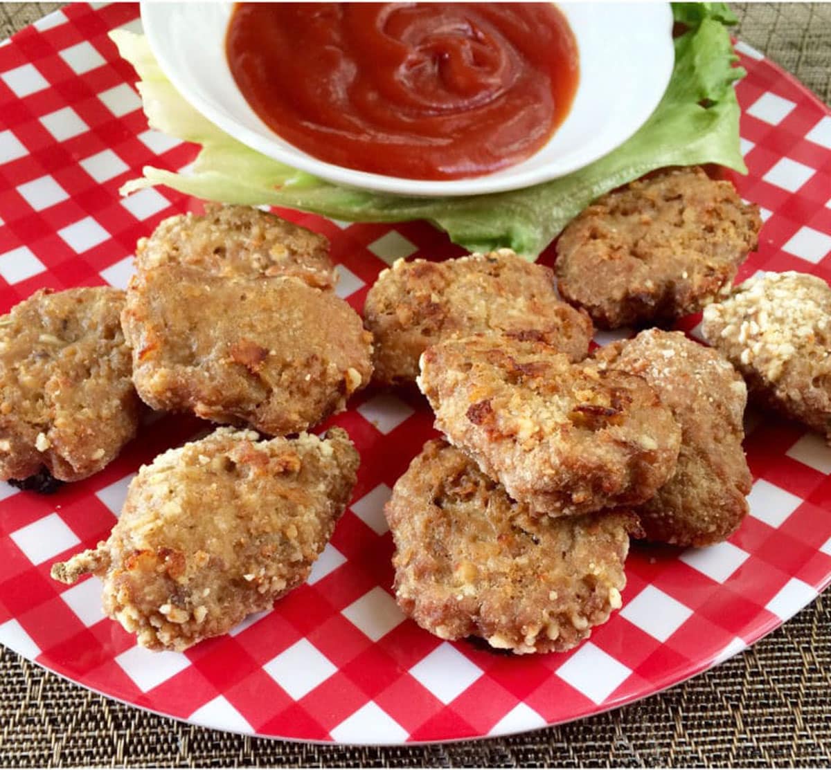 A red checkered plate with a bunch of turkey nuggets and a small white bowl of ketchup.