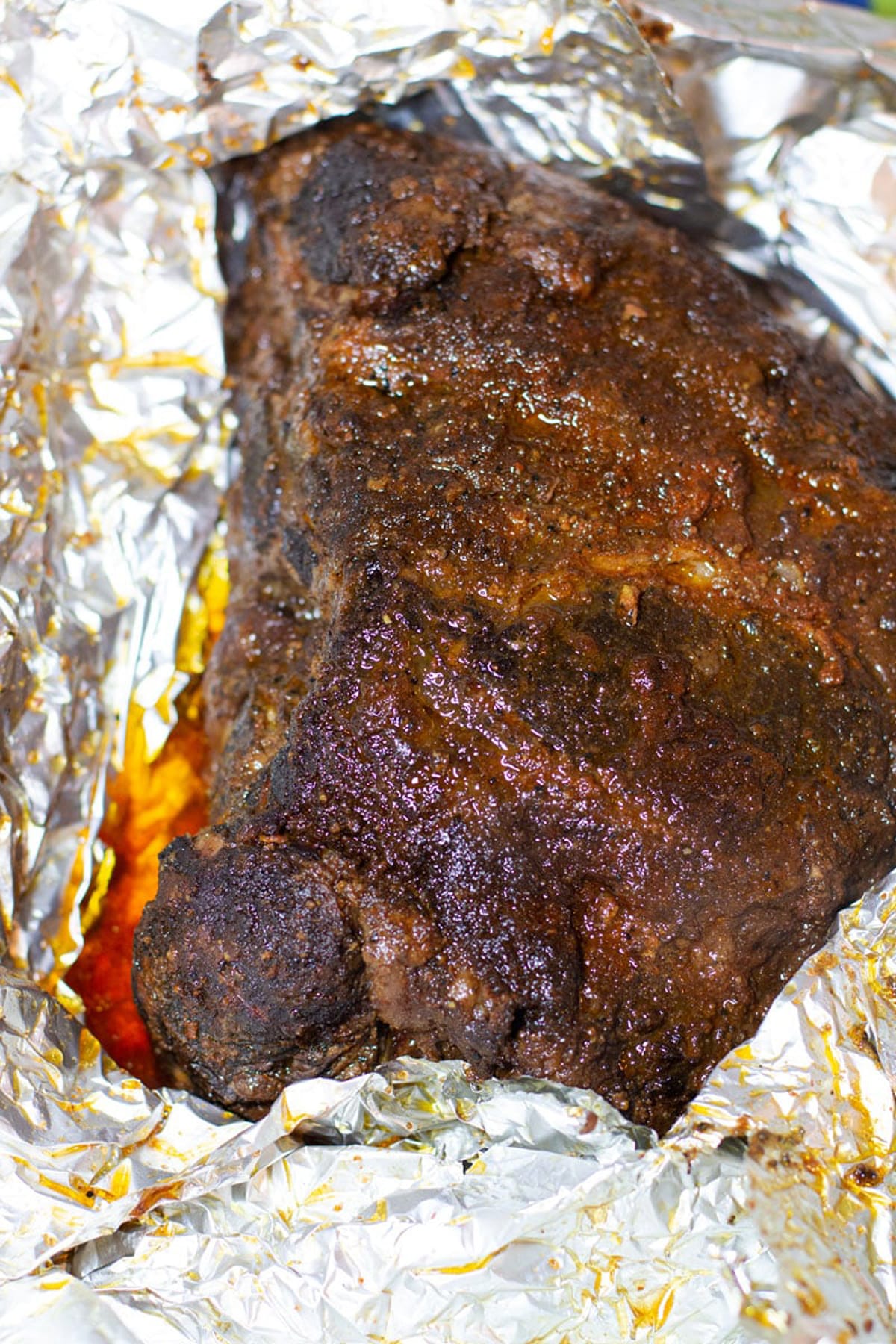 Smoked pork shoulder being unwrapped from an aluminum foil packet.