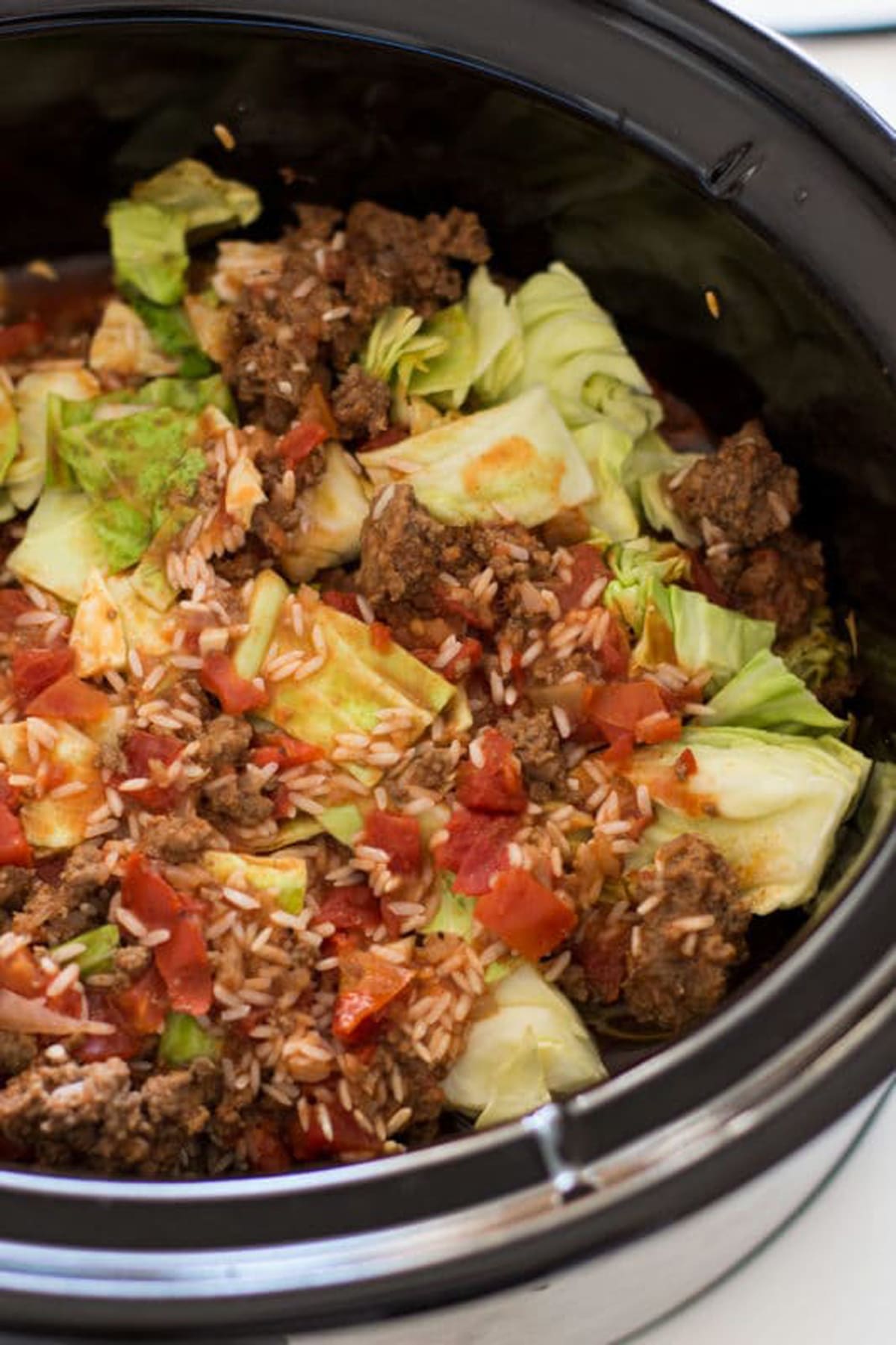 Crock Pot containing ingredients for Cabbage Roll Casserole including cabbage, ground beef, rice and tomatoes. 