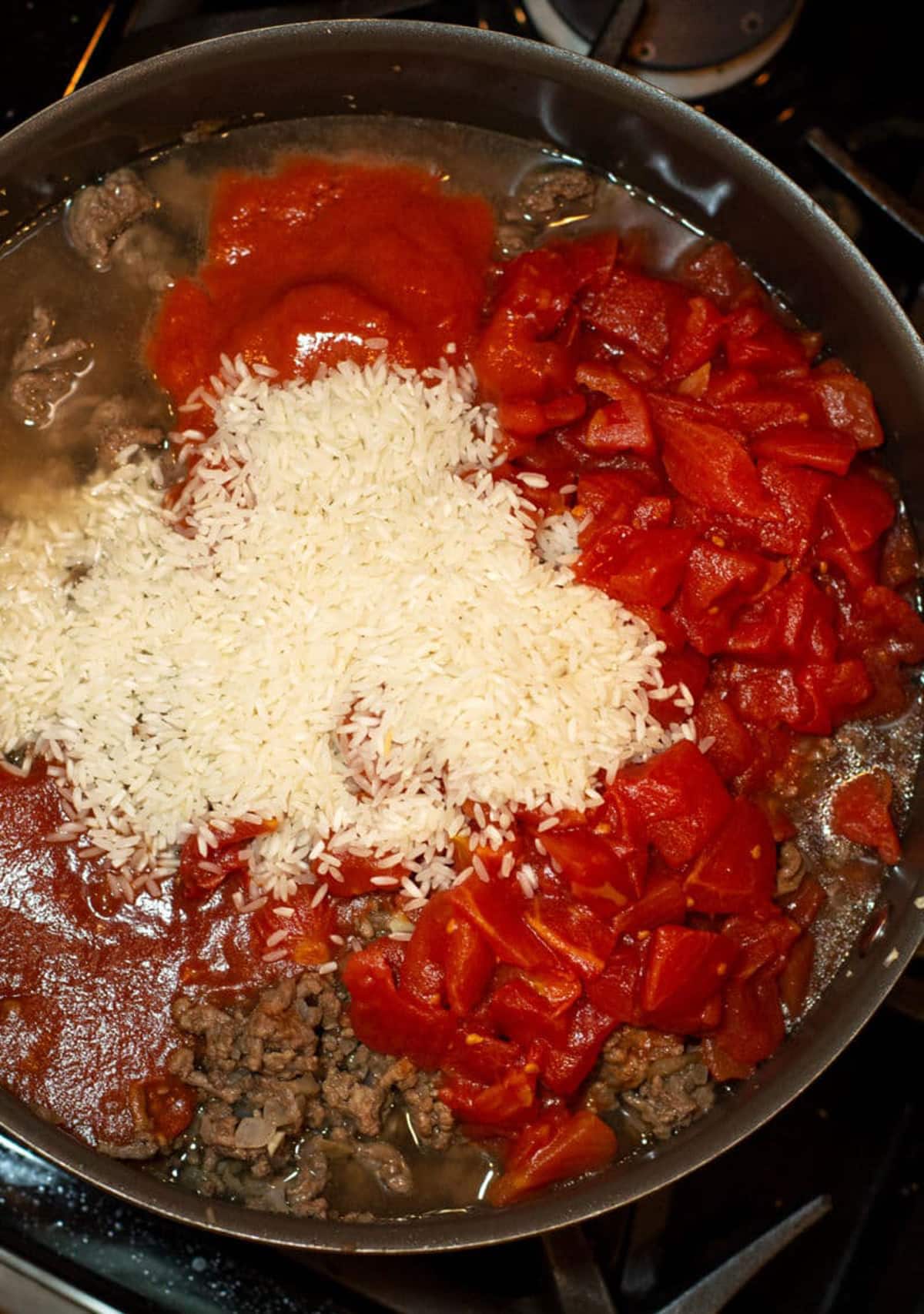 Pot containing diced tomatoes, tomato sauce, rice, and ground beef.
