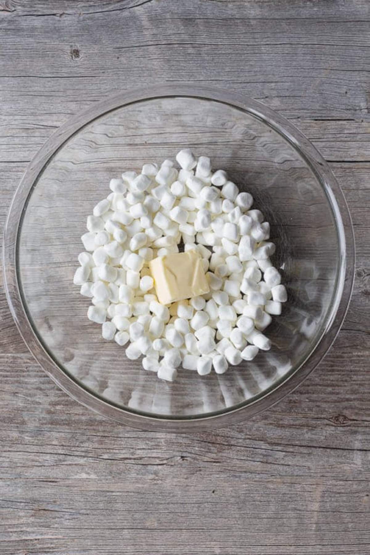 Mini marshmallows and a pat of butter in a large glass bowl.