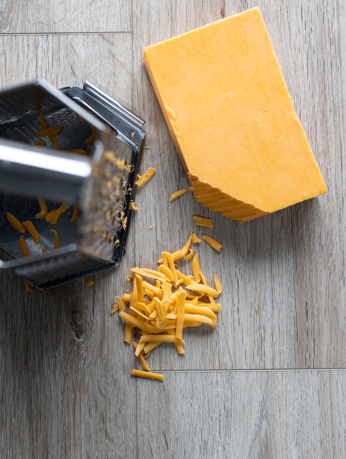 Shredded cheese on counter next to a cheese block and grater. 