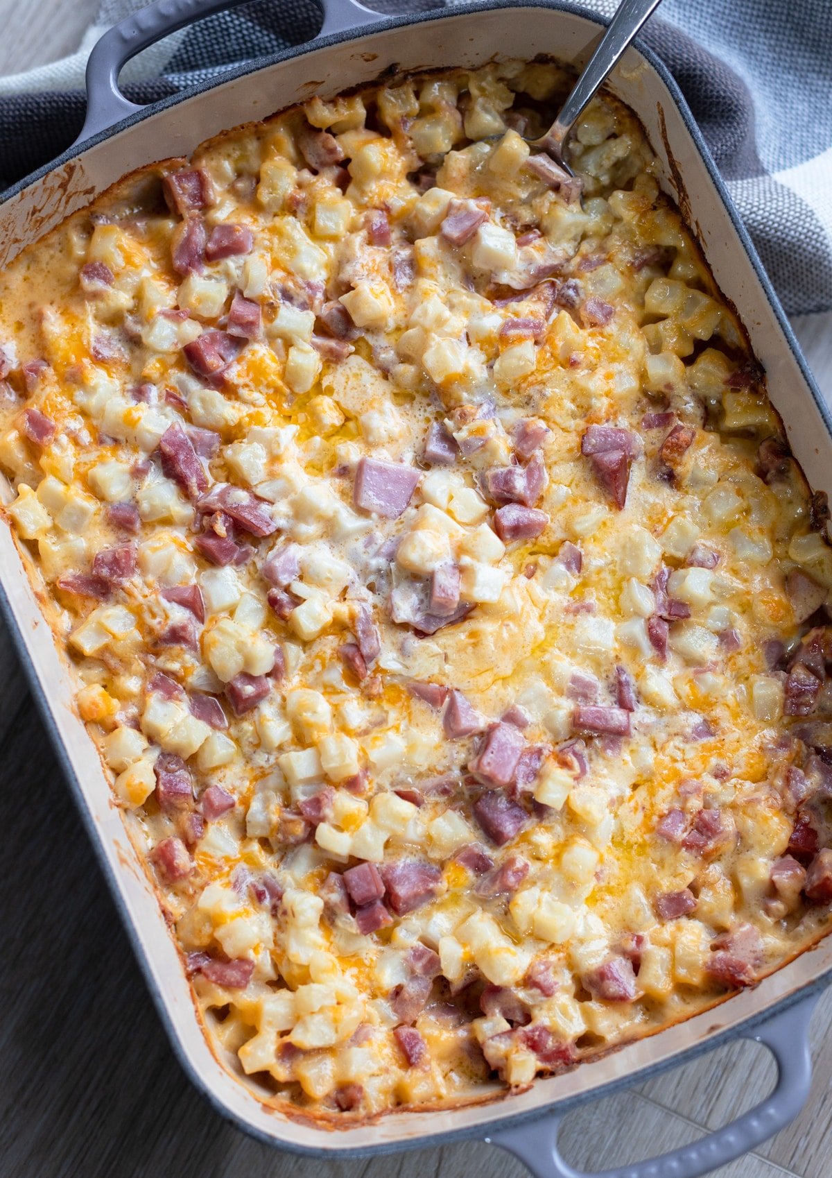 Casserole dish containing baked ham and potato casserole, spoon in dish. 