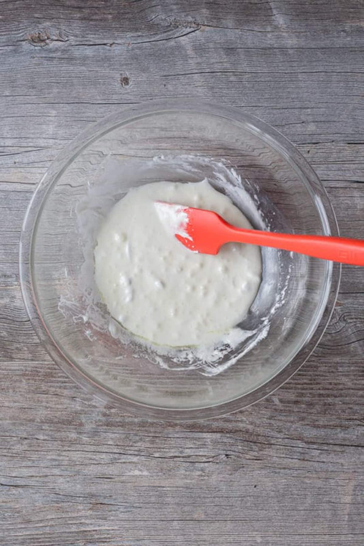 Melted marshmallows and butter in a clear bowl with a red spatula.