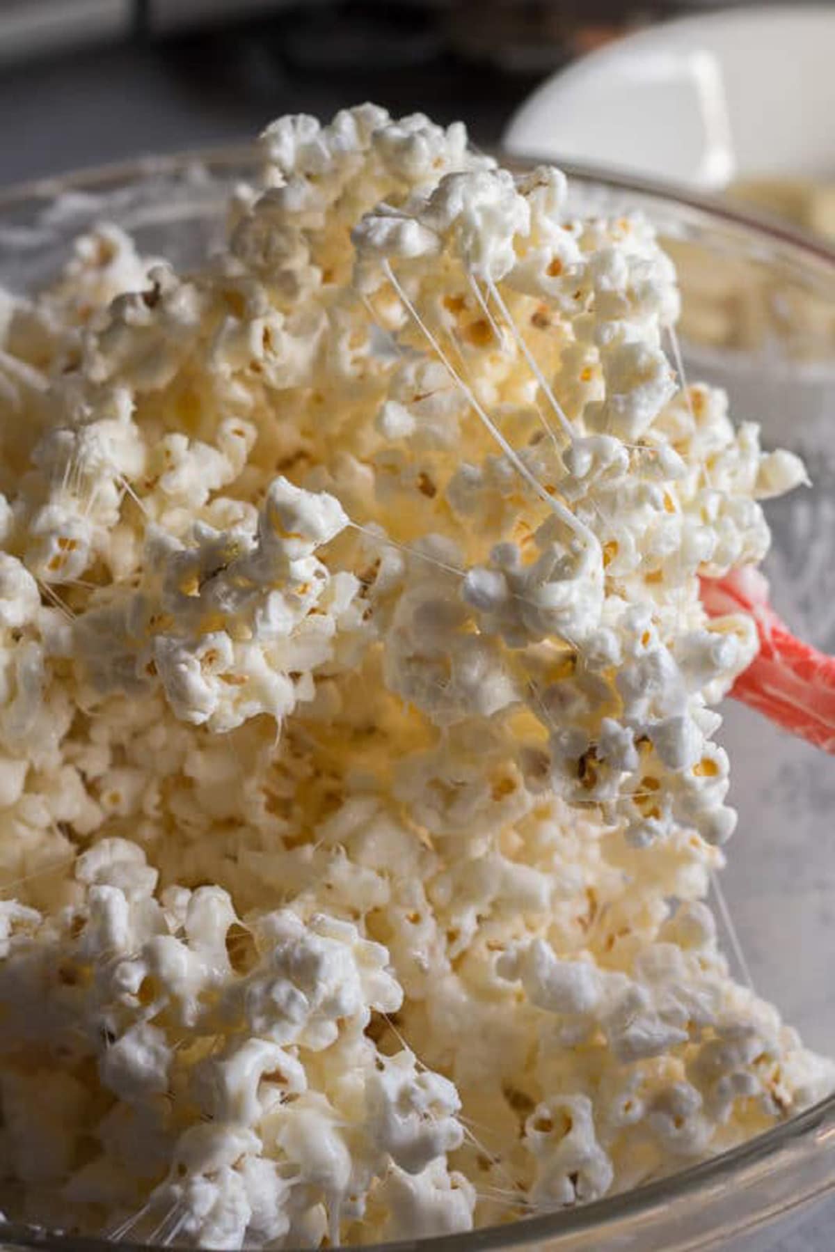 Melted marshmallows being stirred into popcorn with a red spatula.
