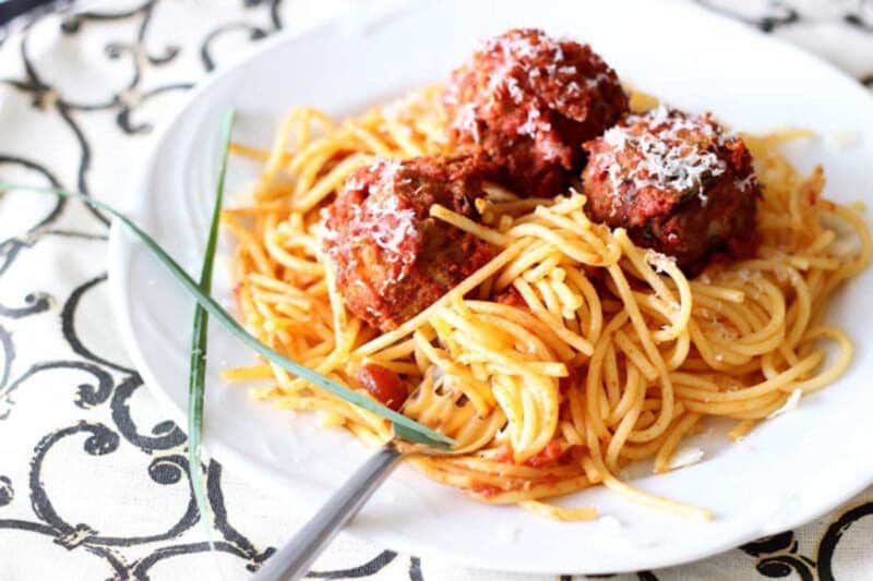 White plate containing spaghetti noodles, three meatballs, and marinara sauce.