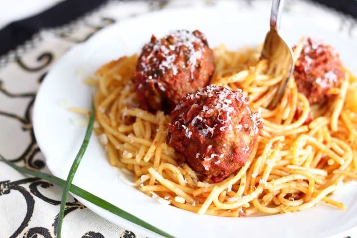 White plate containing spaghetti noodles with 3 meatballs and marinara sauce.